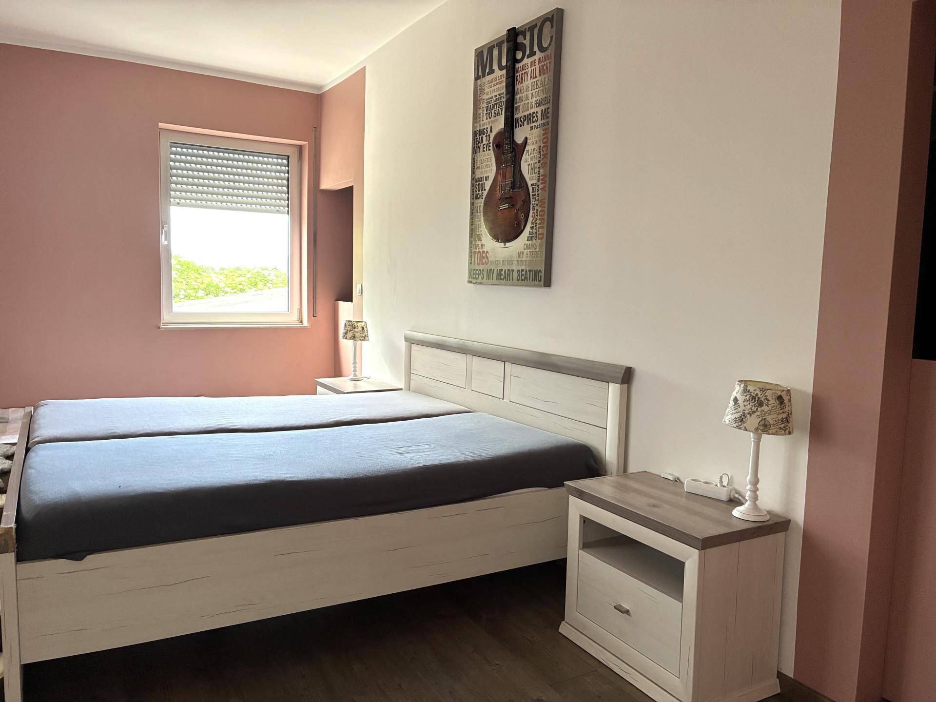 Schlafzimmer mit Doppelbett, Nachttischen und rosafarbenen Akzentwänden.