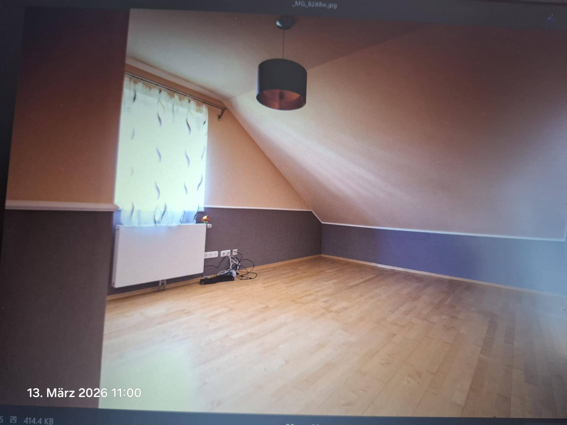 Helles Zimmer im Dachgeschoss mit schrägen Wänden, Holzfußboden und einem Fenster.