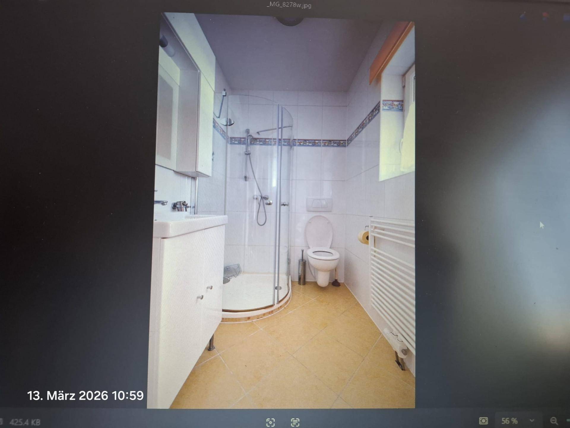 Badezimmer mit Duschkabine, WC, Waschbecken und Fenster, ausgestattet mit hellen Fliesen.