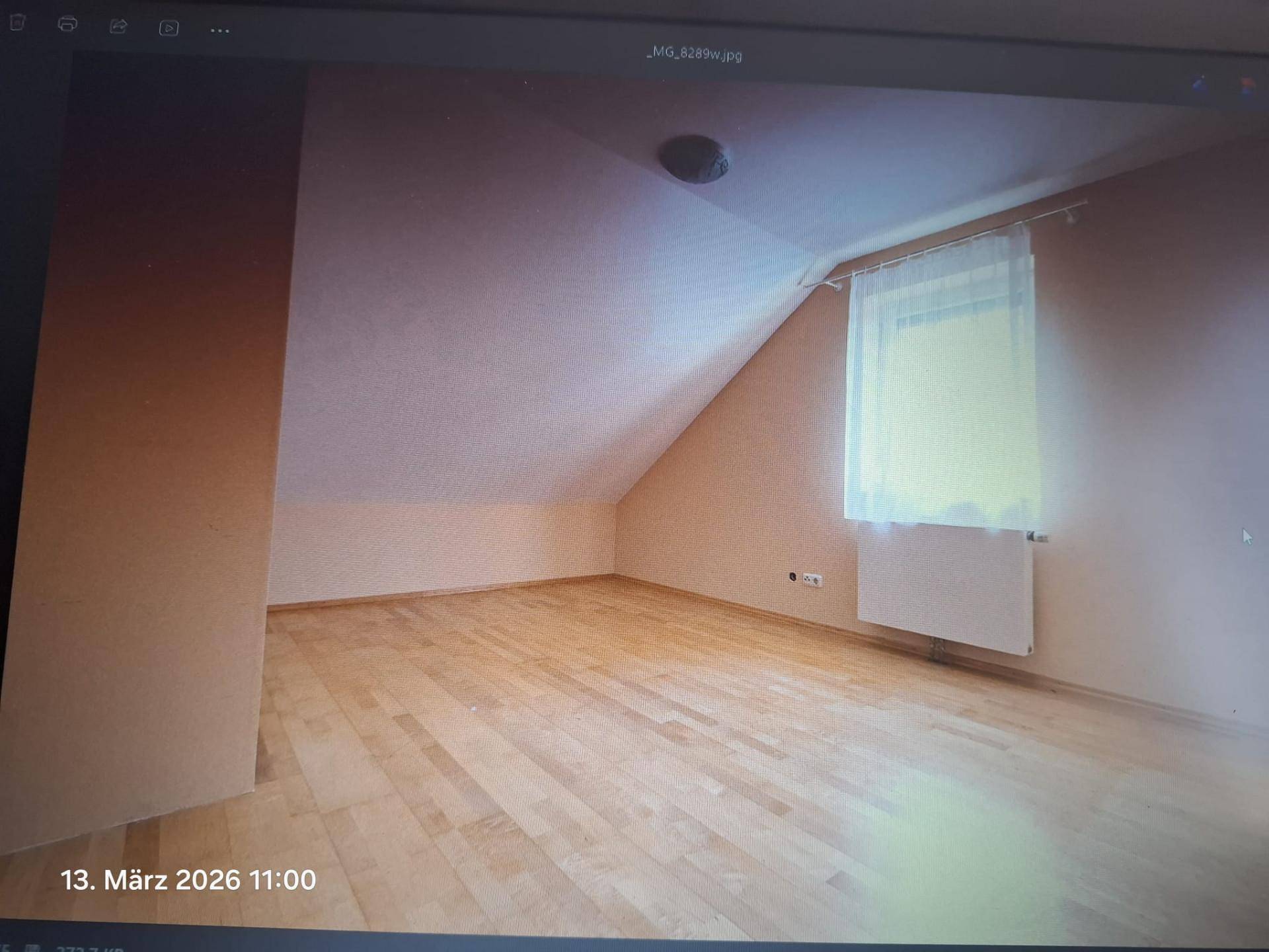 Geräumiges Zimmer im Dachgeschoss mit schrägen Wänden, Holzfußboden und einem Fenster.
