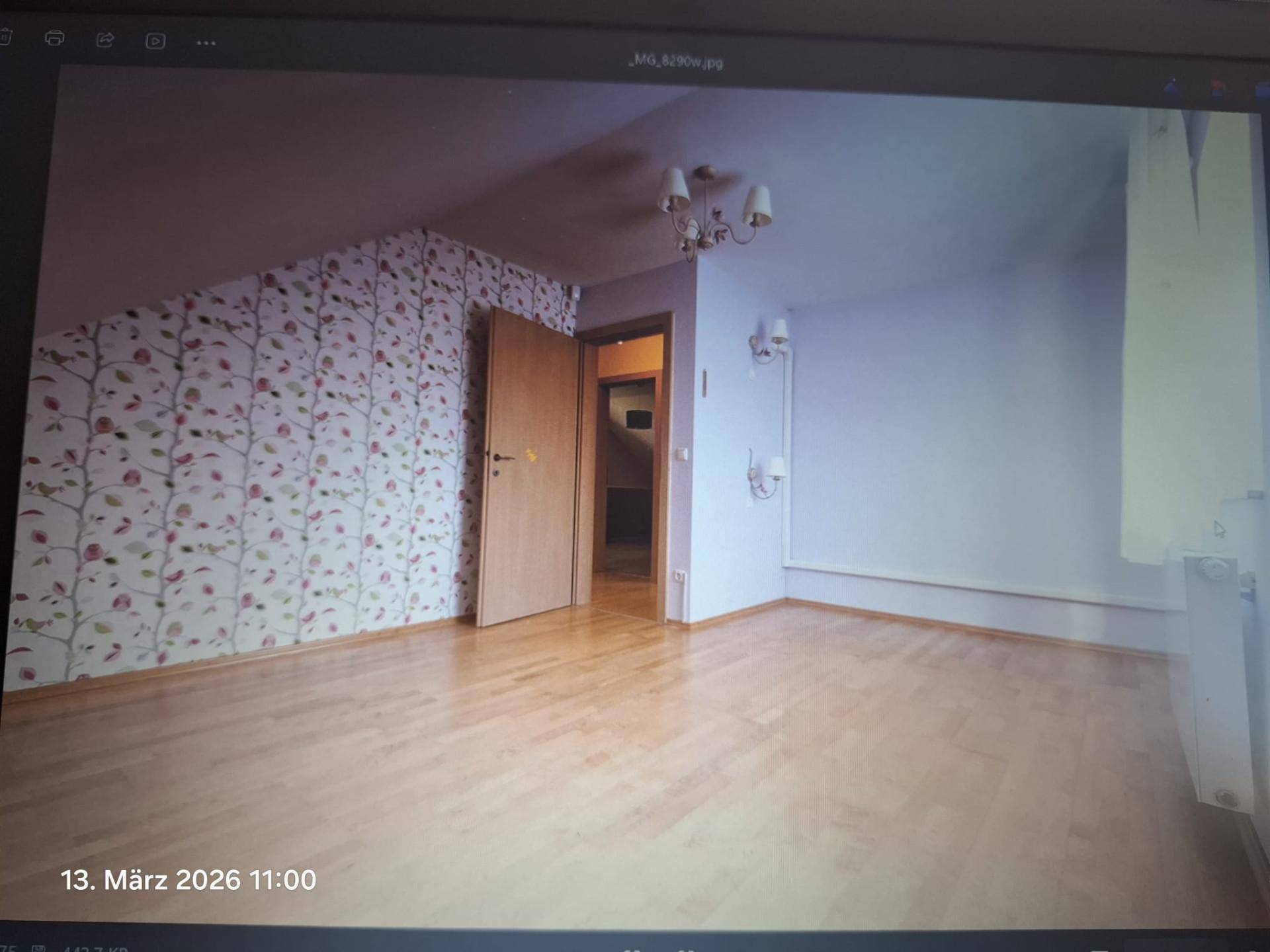 Dachgeschosszimmer mit Holzboden, floraler Tapete und einer Tür, die zu einem Flur führt.