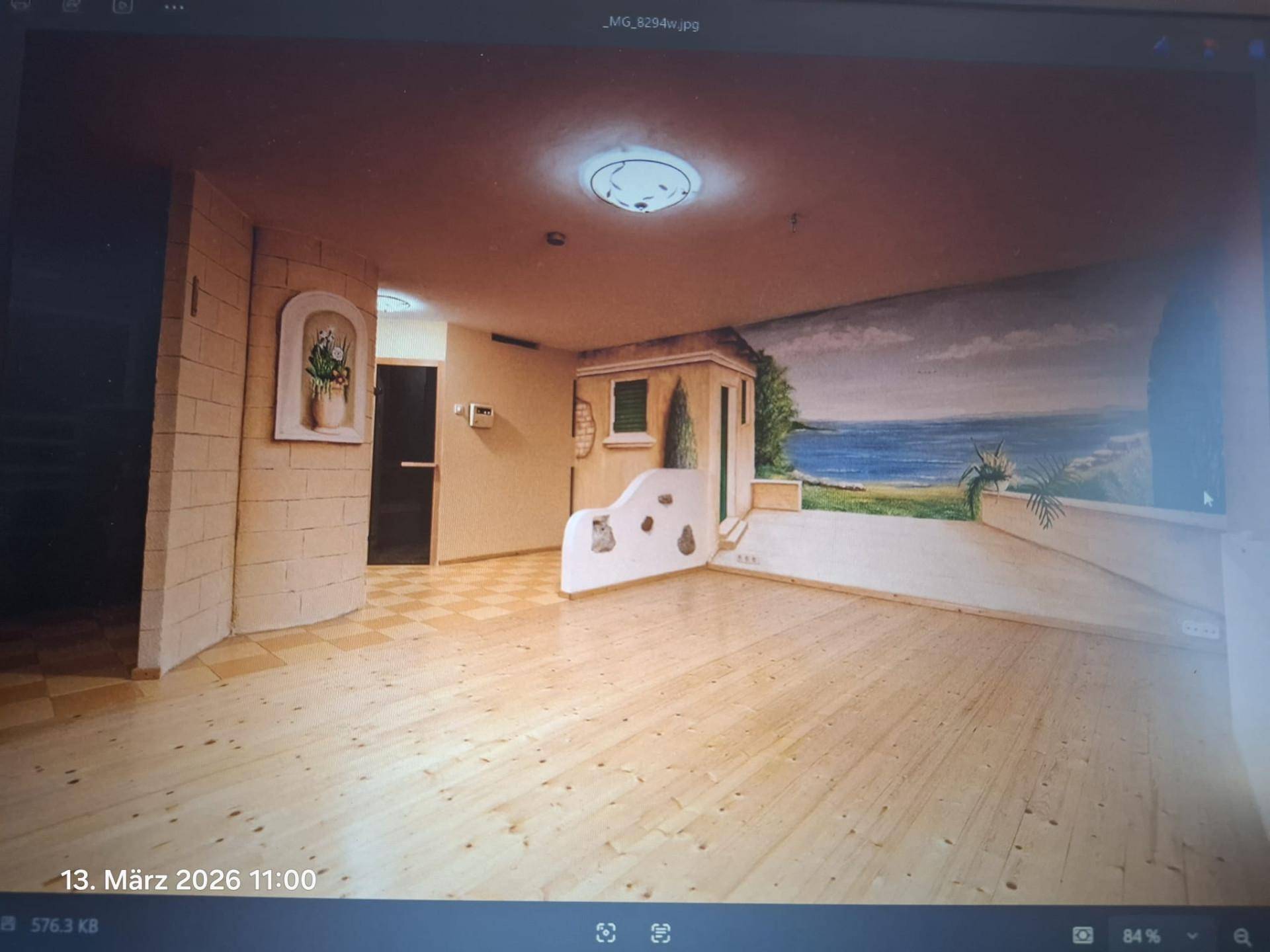 Raum mit Holzboden und einer Wandmalerei, die eine mediterrane Küstenlandschaft darstellt.