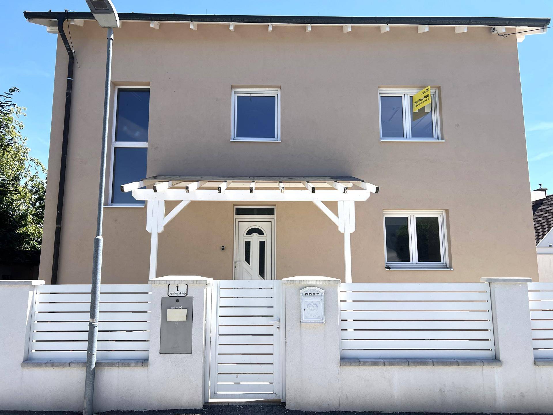 Vorderansicht eines modernen Hauses mit Eingangsbereich, weißer Pergola und gepflegtem Vorgarten.