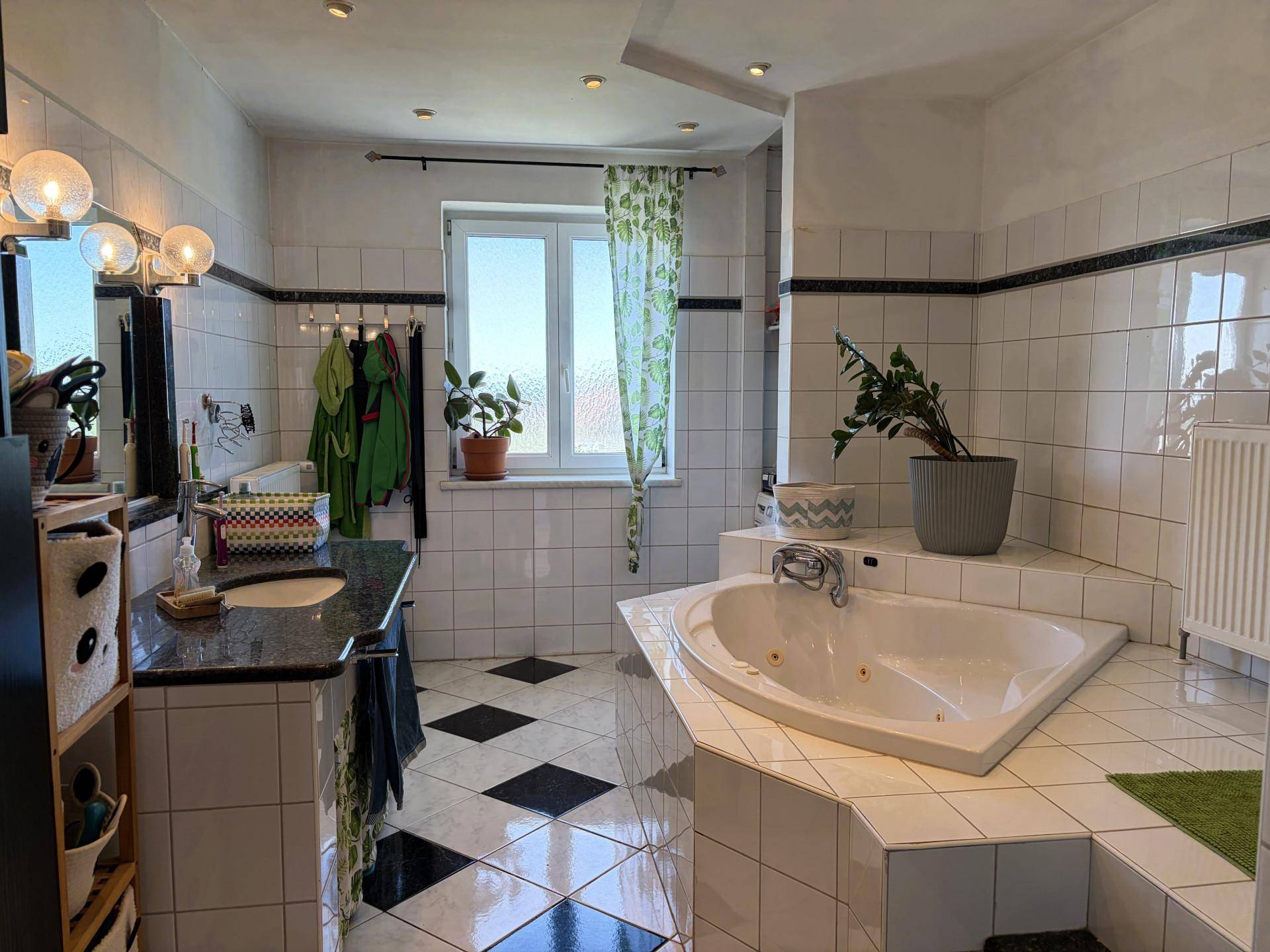 Geräumiges Badezimmer mit Eckbadewanne, schwarzen und weißen Fliesen und Fenster.