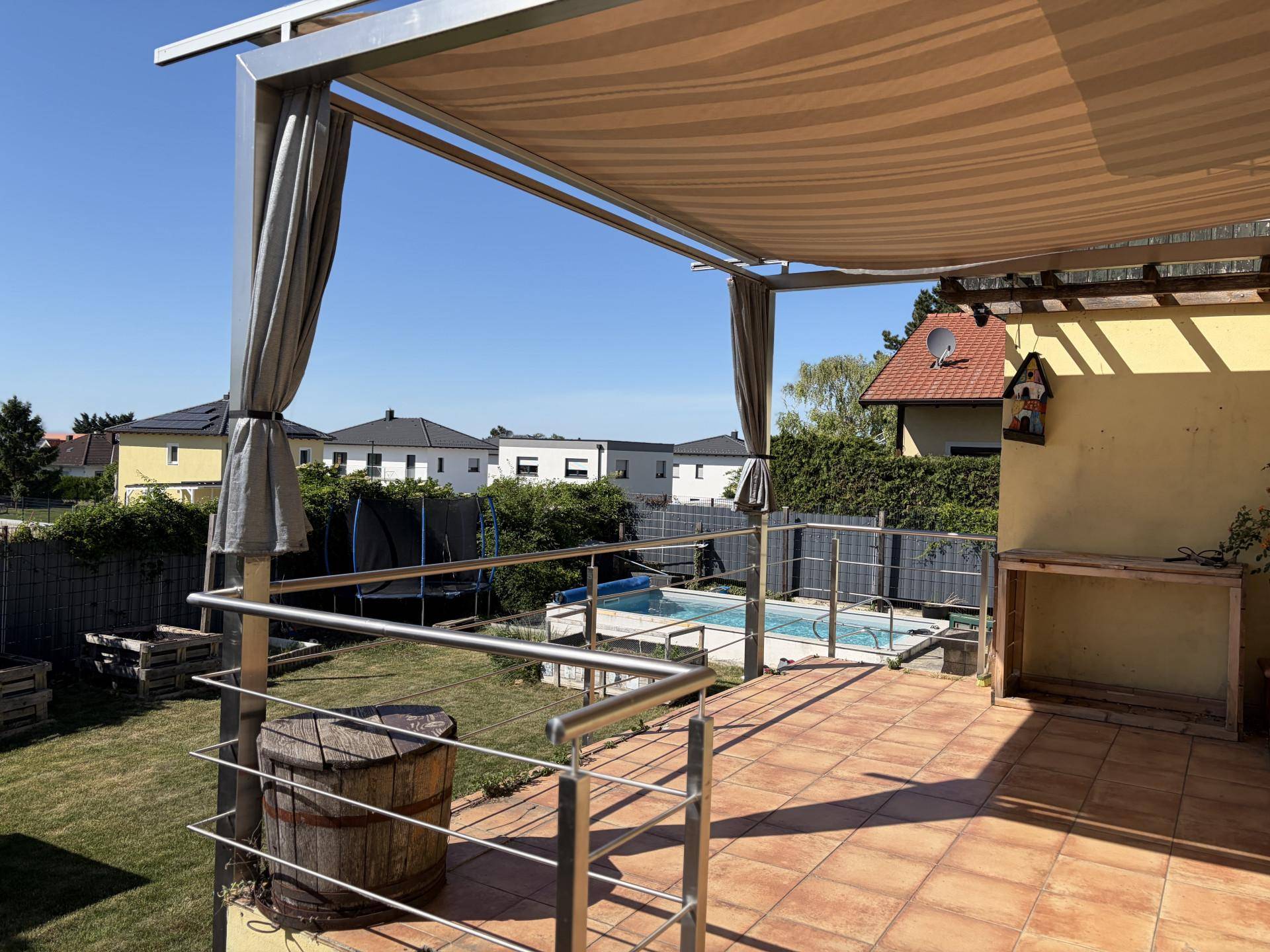 Überdachte Terrasse mit Fliesenboden, Metallgeländer und Blick auf den Garten und Pool.