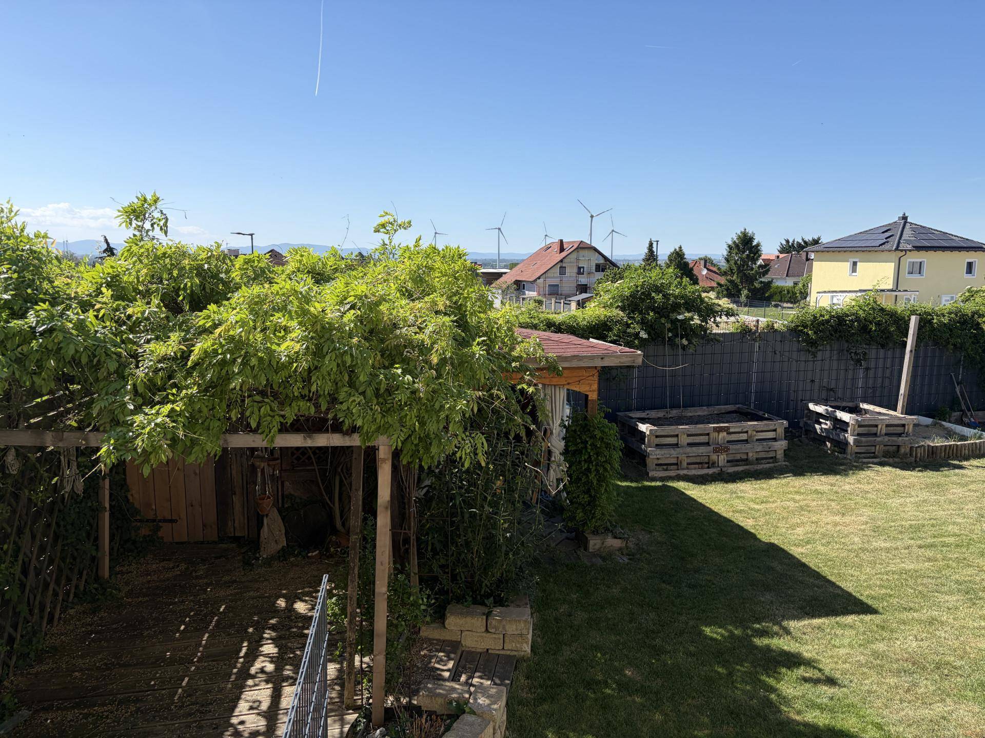Grüner Gartenbereich mit Bäumen, Hochbeeten und weitem Blick in die Ferne.