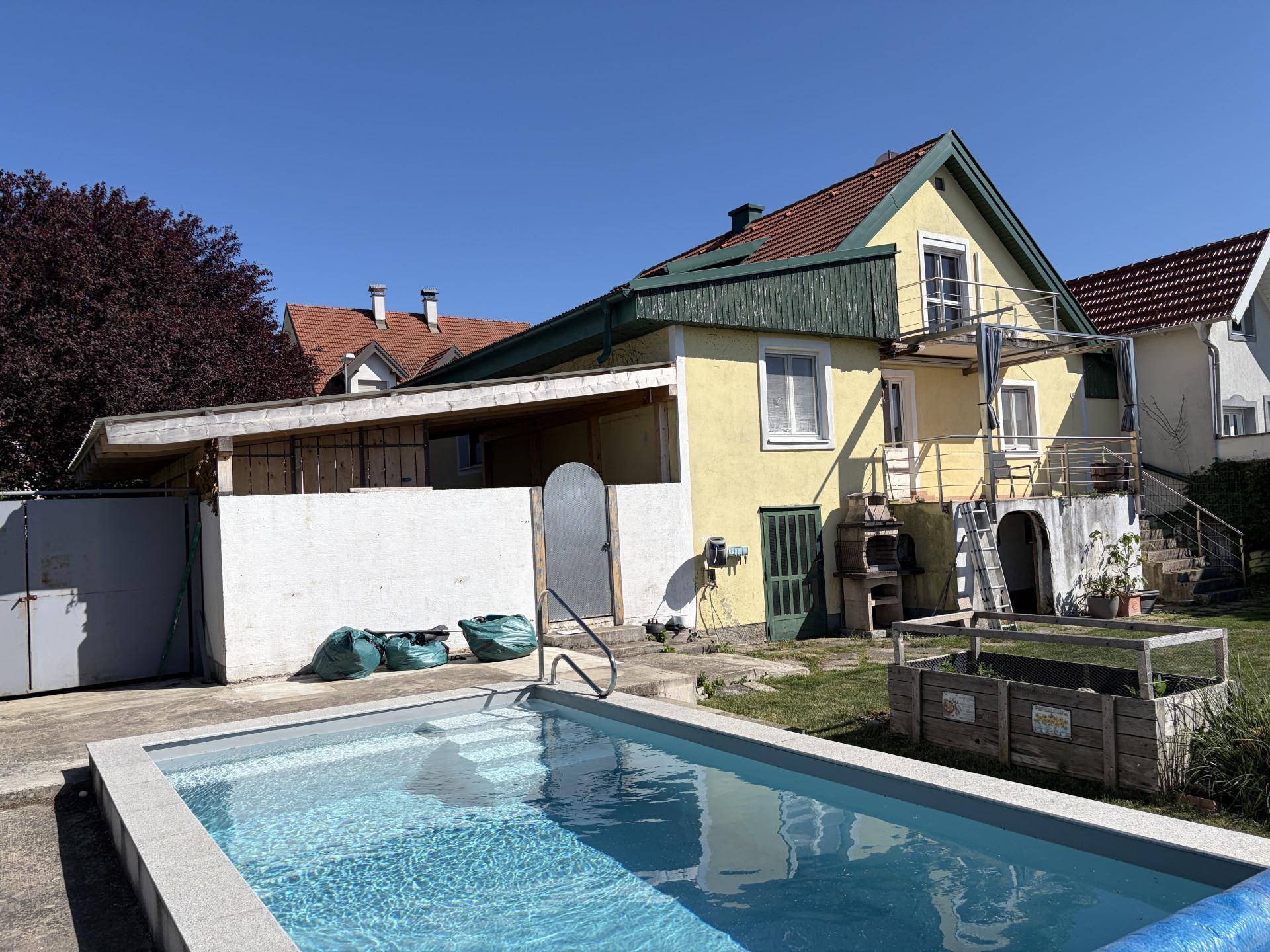 Hausansicht von hinten mit Pool im Vordergrund und angrenzendem Carport.