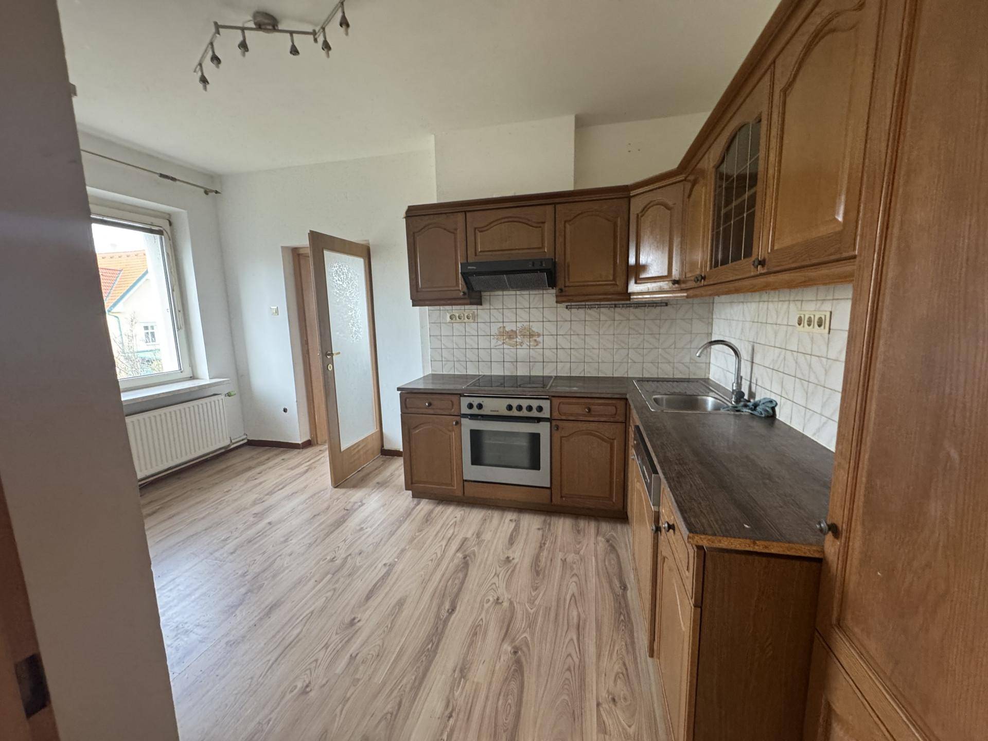 Küche mit traditionellen Holzschränken, Einbauherd und Spüle, ausgestattet mit Laminatboden.