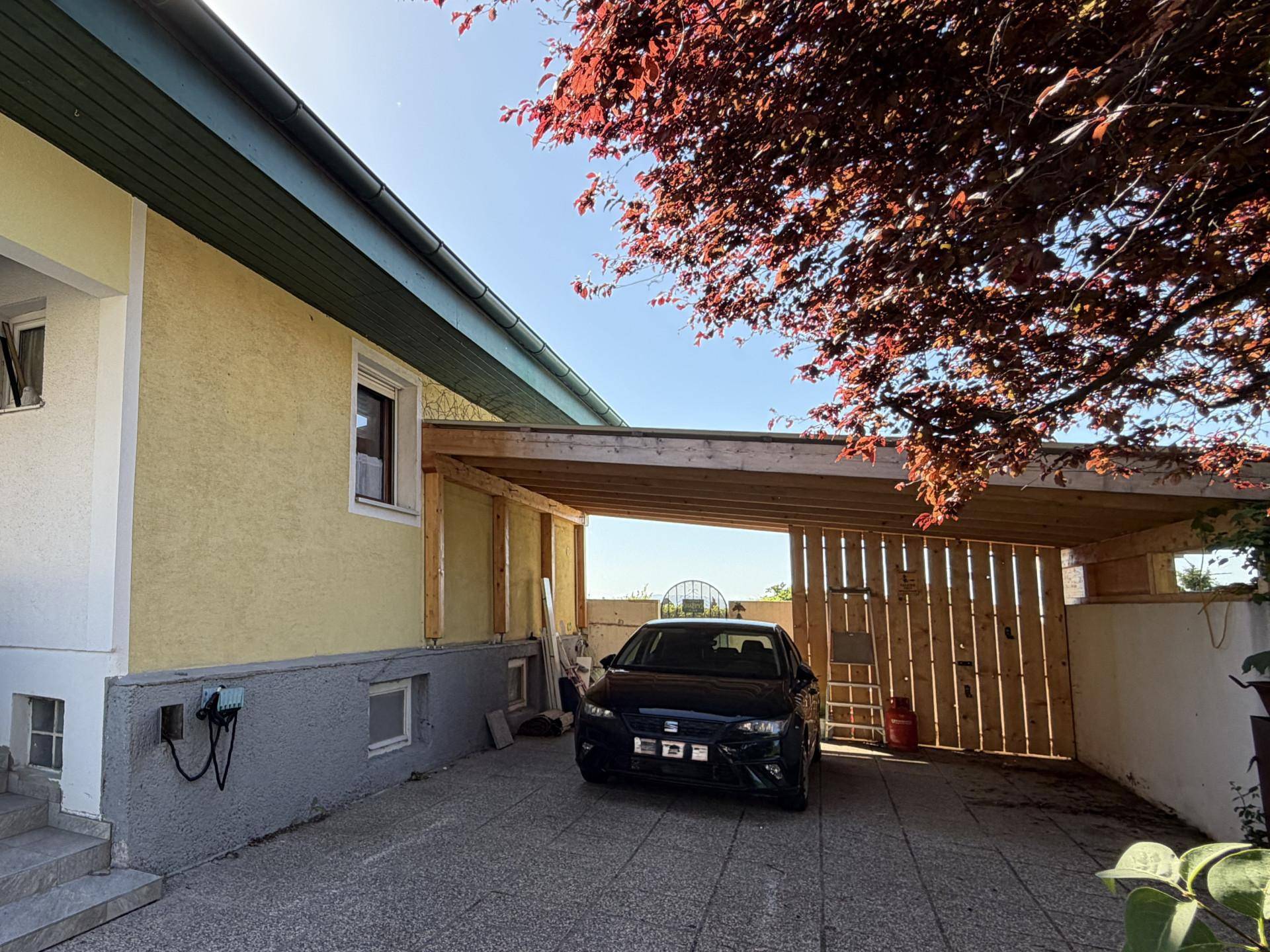 Carport mit gepflasterter Einfahrt und einem geparkten Auto vor dem Haus.