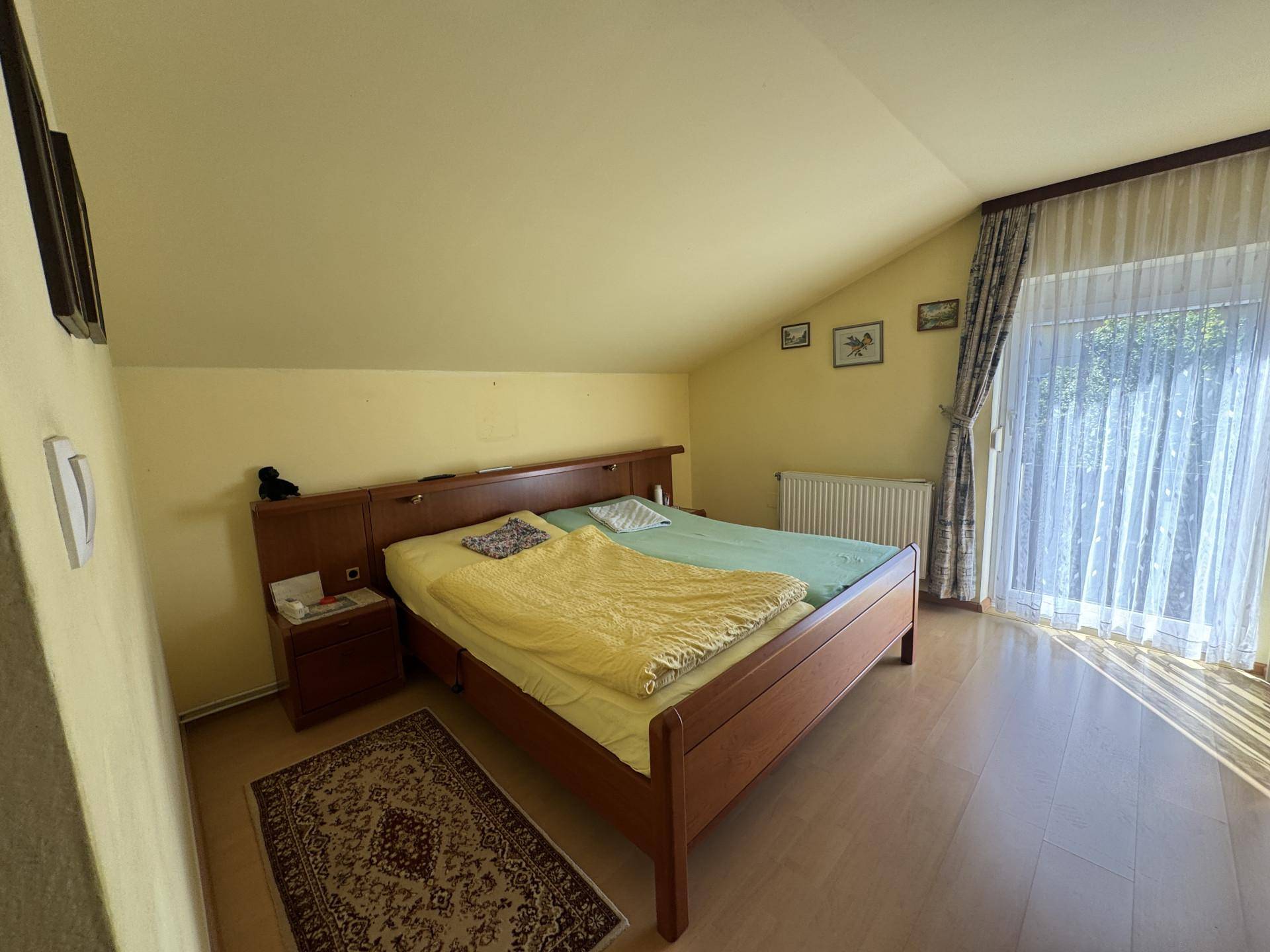 Geräumiges Schlafzimmer im Dachgeschoss mit Doppelbett, Dachschräge und Zugang zum Balkon.