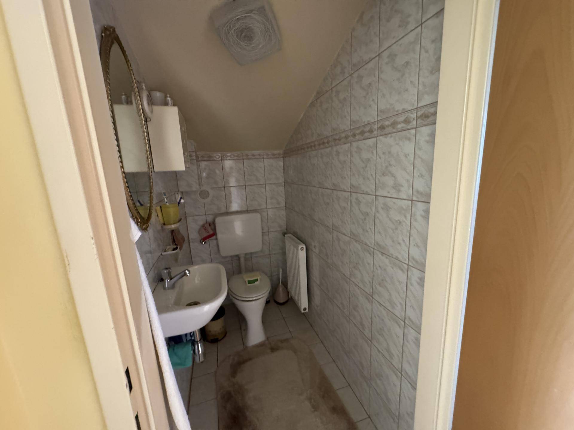 Kleines Gäste-WC mit Dachschräge, hellen Fliesen und Einzelwaschbecken.
