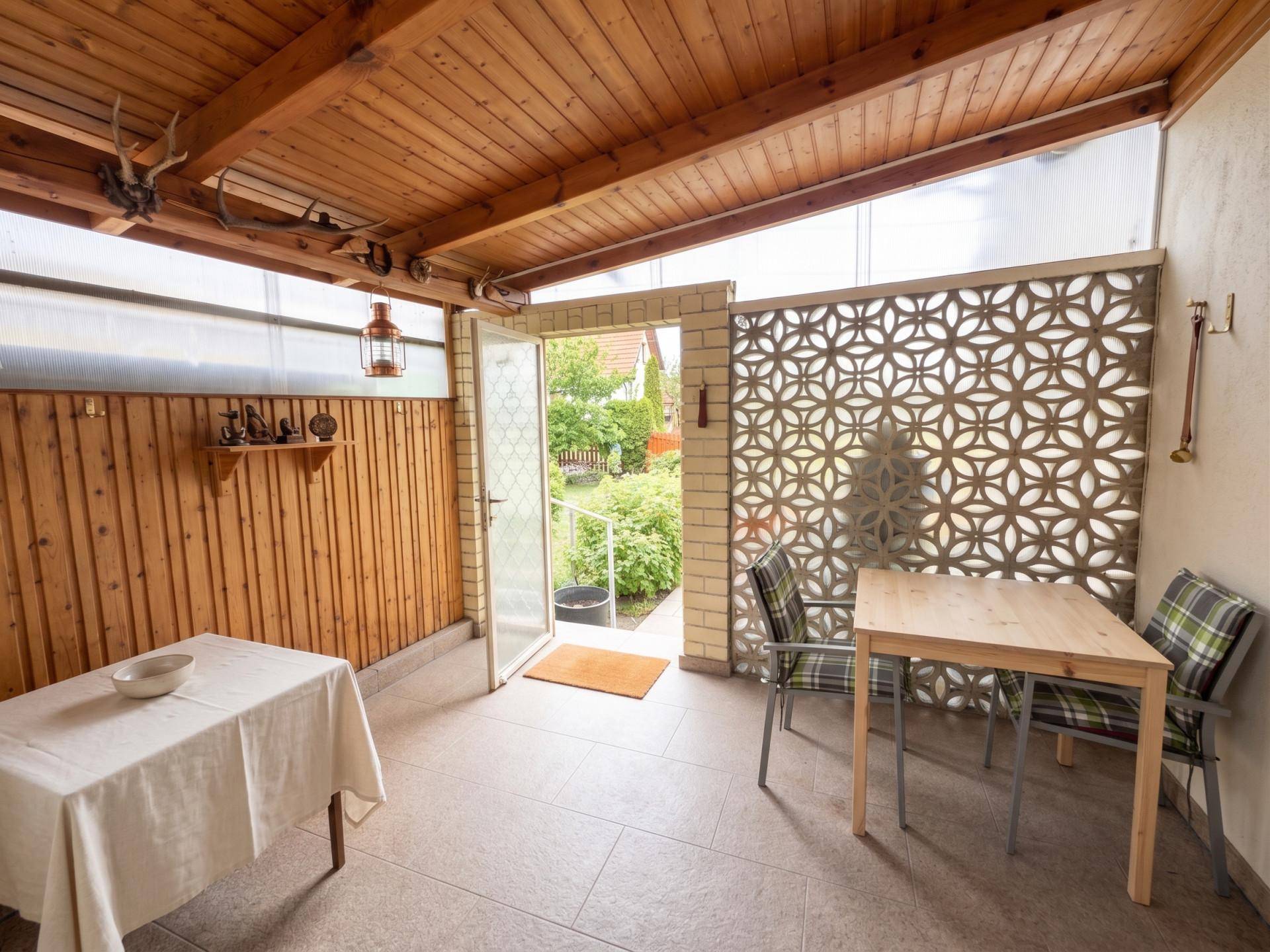 Überdachte Loggia mit Holzbalkendecke, Fliesenboden und Zugang zum Garten.