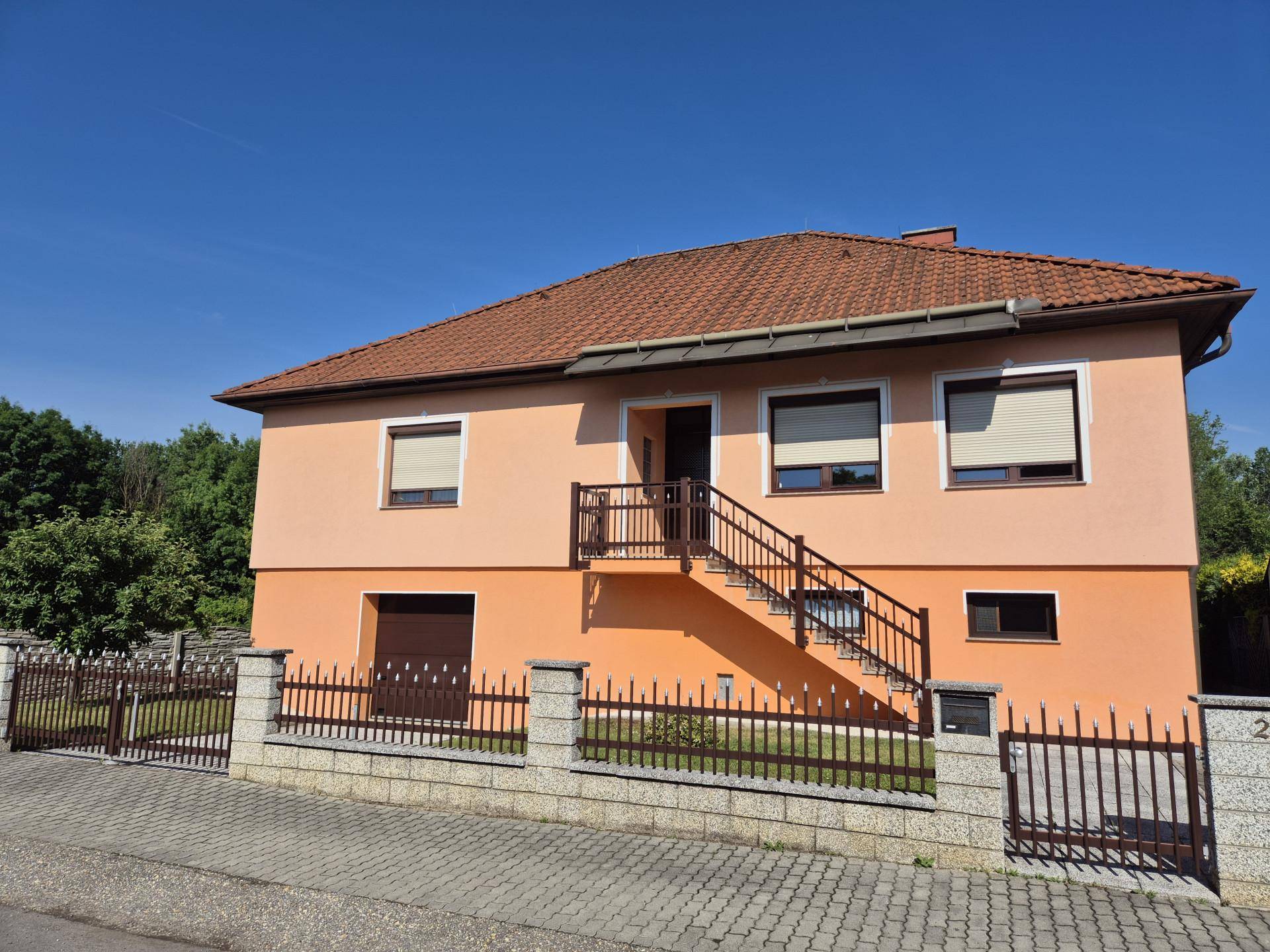 Vorderansicht des Hauses mit Außentreppe, Zaun und gepflegtem Vorgarten.