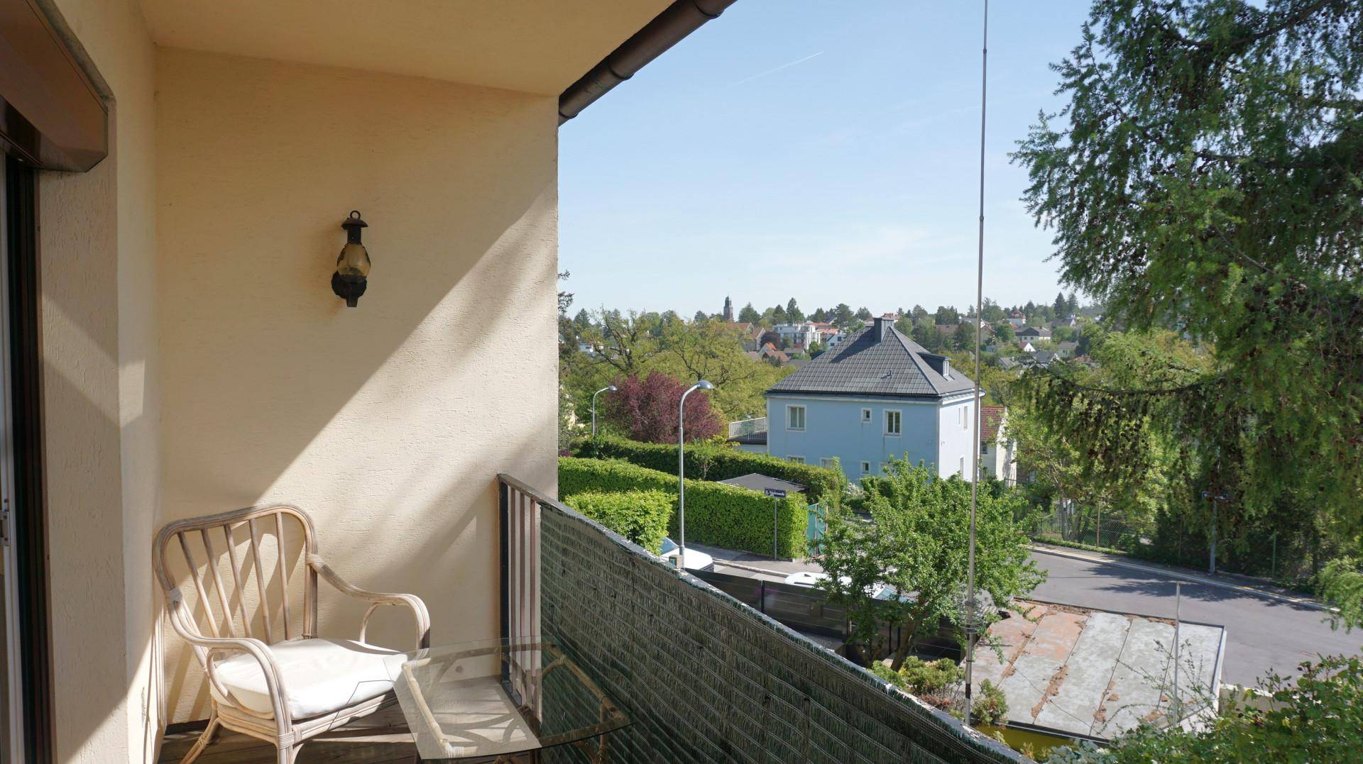 Balkon mit Korbstuhl und weitem Blick über die umliegende Wohngegend und grüne Landschaft.