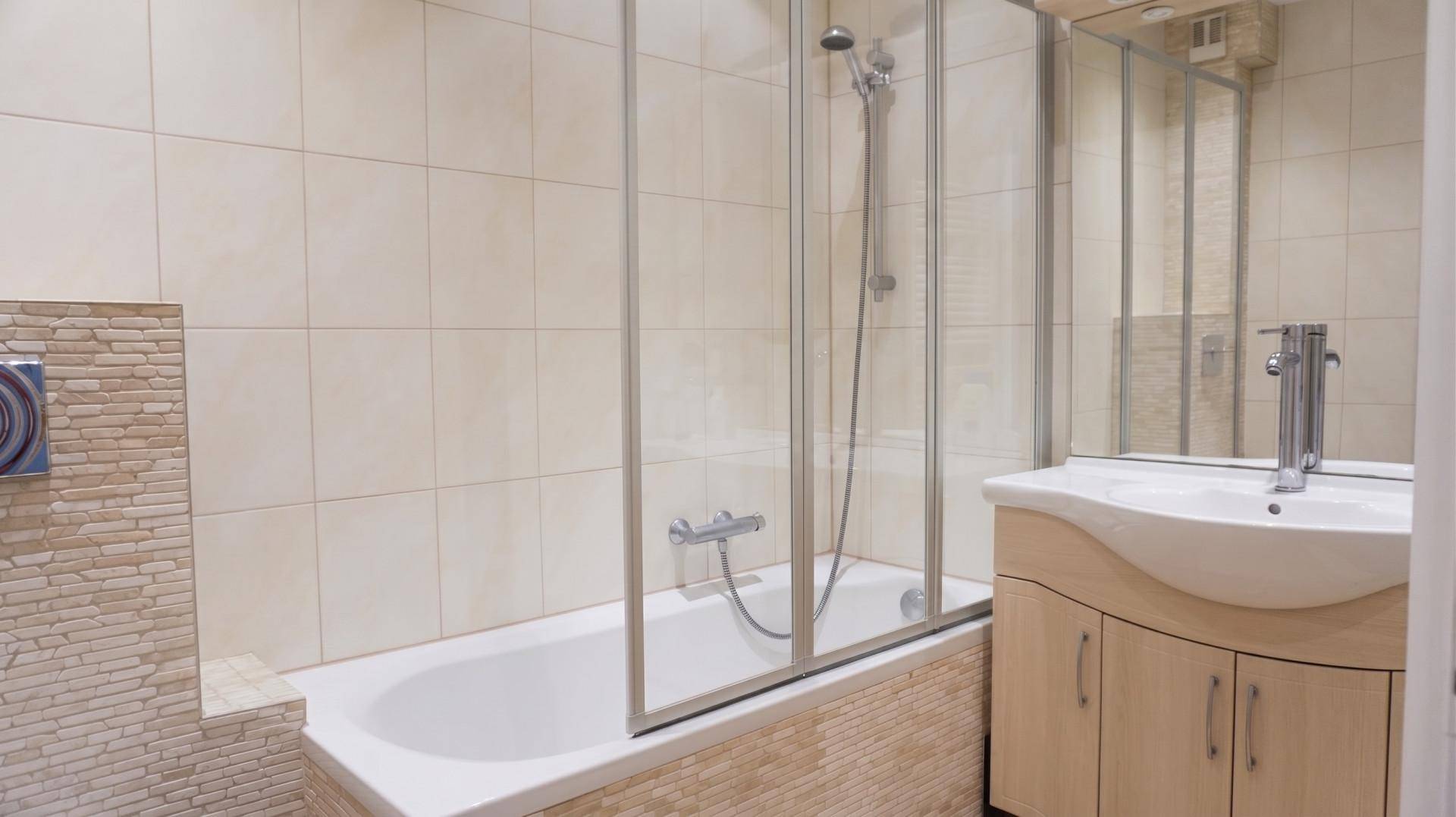 Modernes Badezimmer mit Badewanne, Duschabtrennung und Waschtisch mit hellen Fliesen.