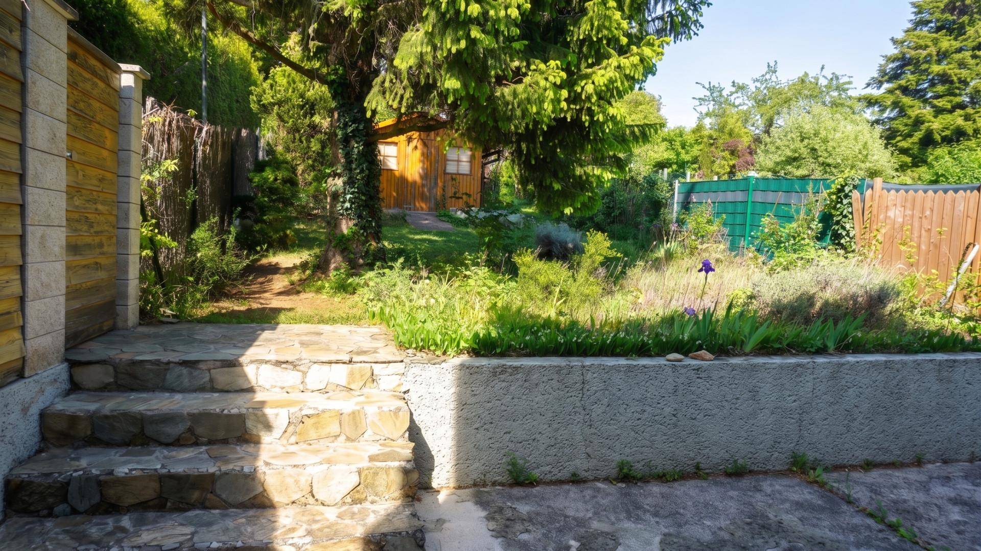 Gartenbereich mit Steinstufen, Rasen und Blick auf einen Holzschuppen im Hintergrund.