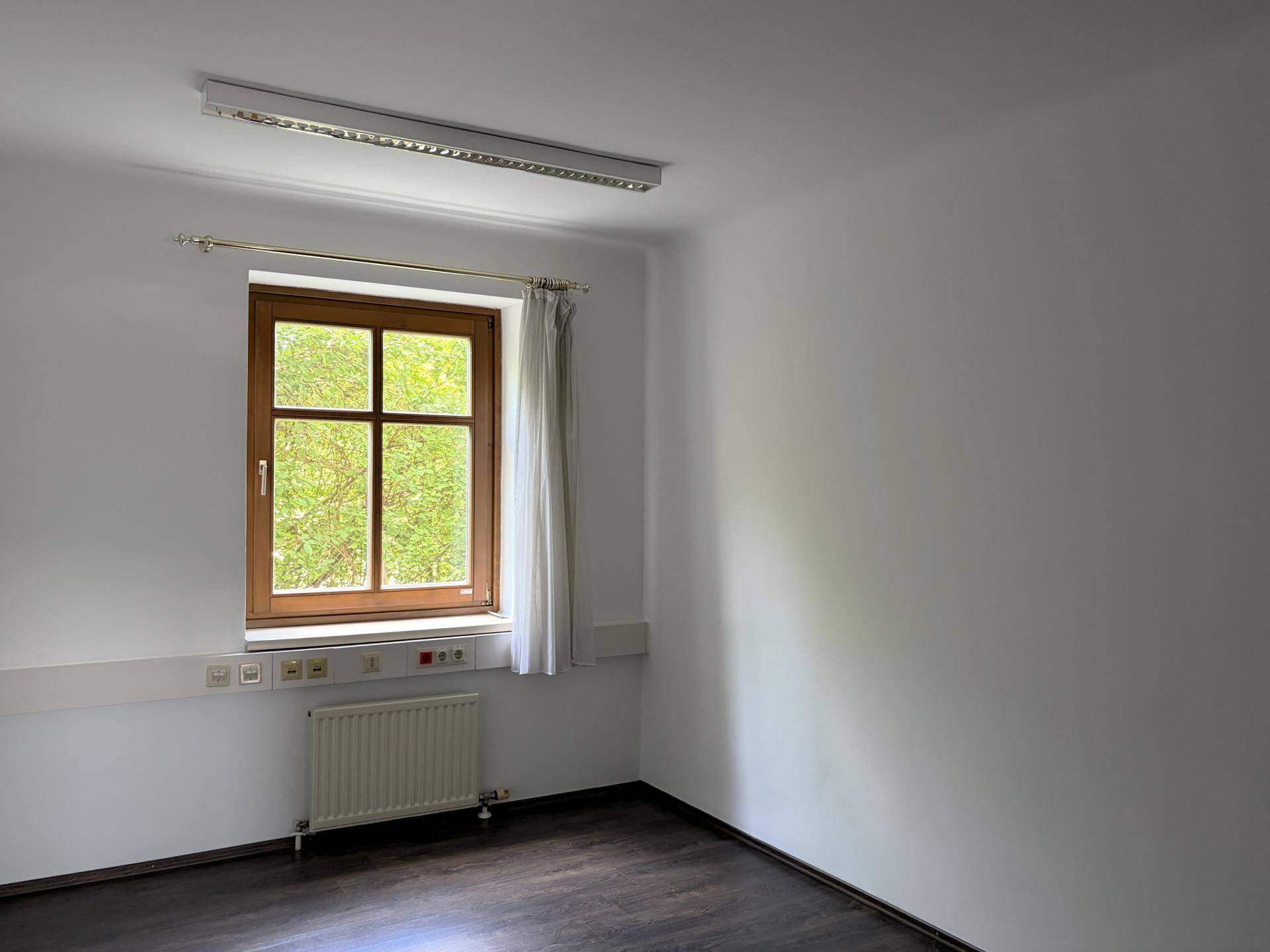 Einzelner Raum mit großem Fenster, dunklem Boden und weiß gestrichenen Wänden, gut beleuchtet.