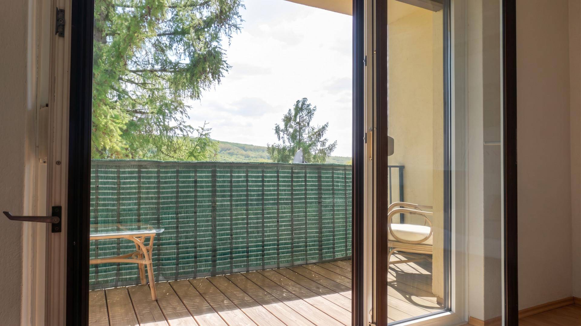 Blick vom Innenraum durch große Glastüren auf den Balkon mit Holzboden und Sichtschutz.