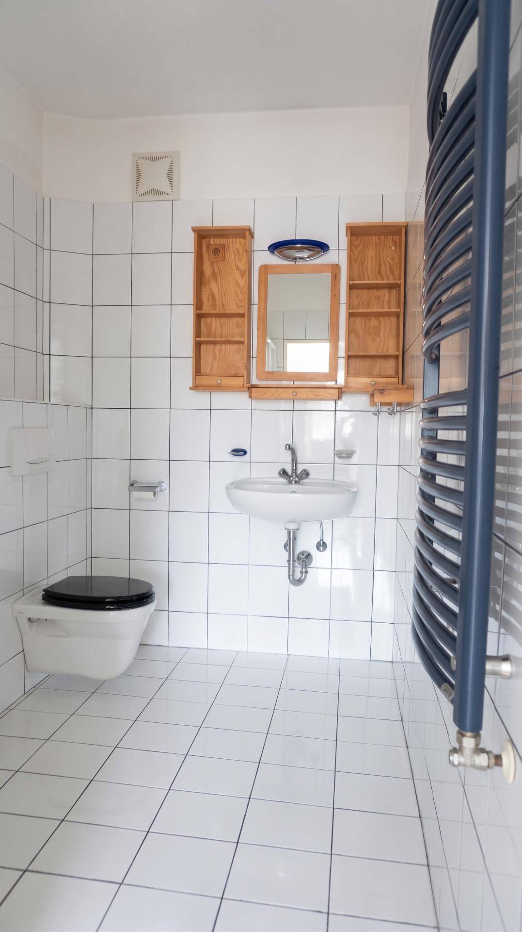 Separates WC mit wandhängender Toilette, Waschbecken und blauem Handtuchheizkörper an der Wand.