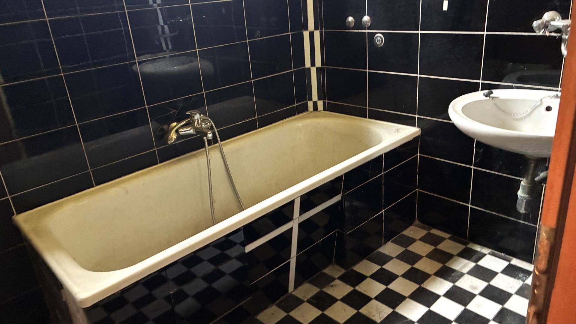 Badezimmer mit schwarzen Fliesen, einer Badewanne und einem Waschbecken im älteren Stil.