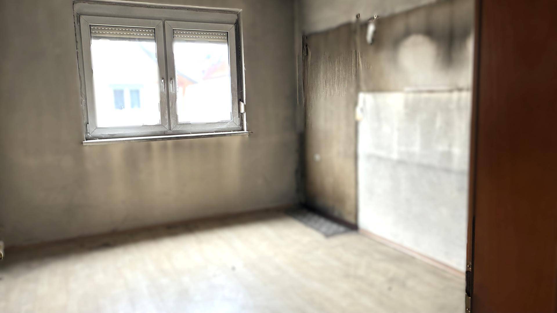 Unmöblierter Raum mit Fenster und abgenutzten Wänden, der eine Renovierung erfordert.