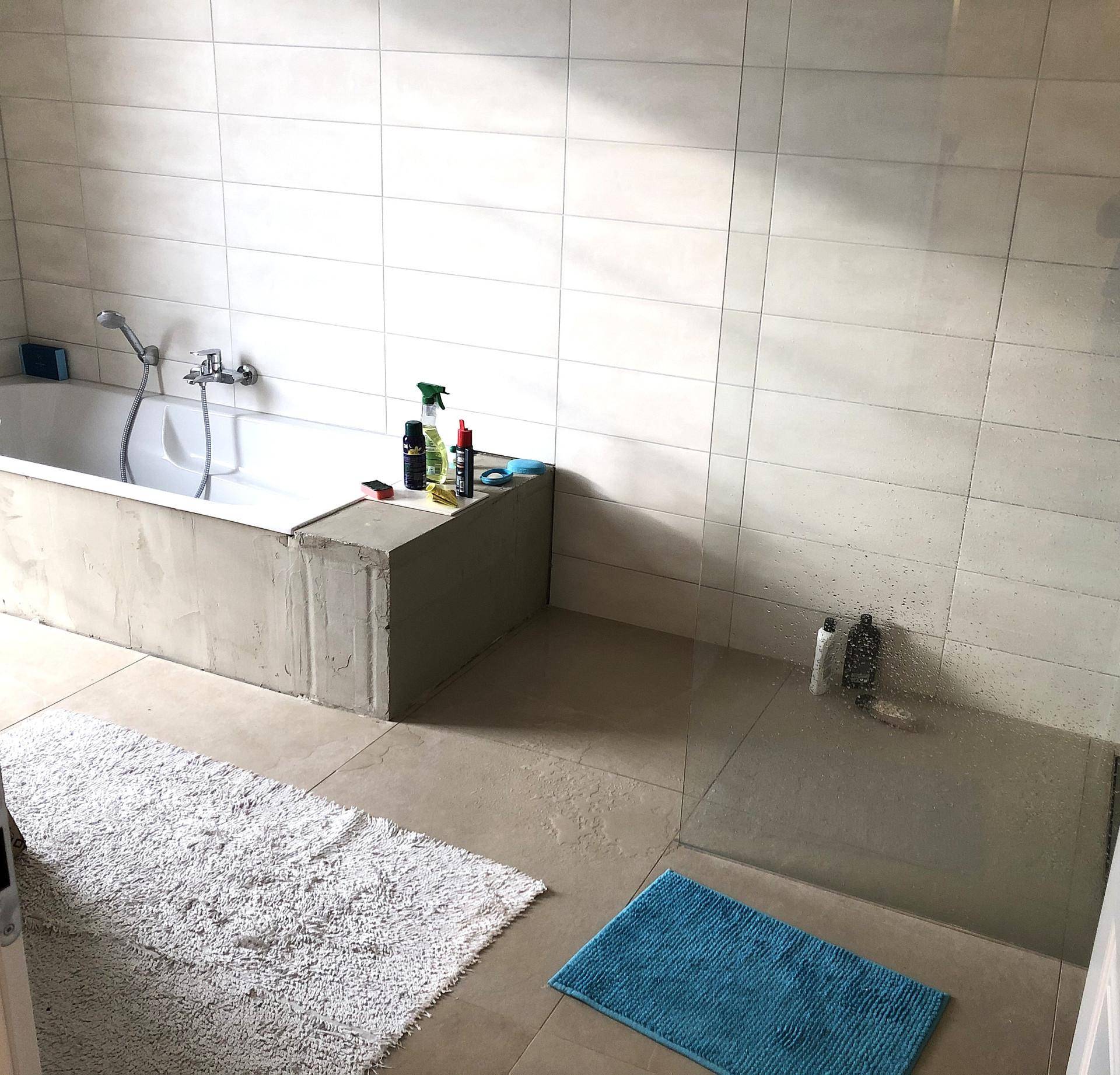 Helles Badezimmer mit Badewanne, großen Fliesen und schlichtem Design.