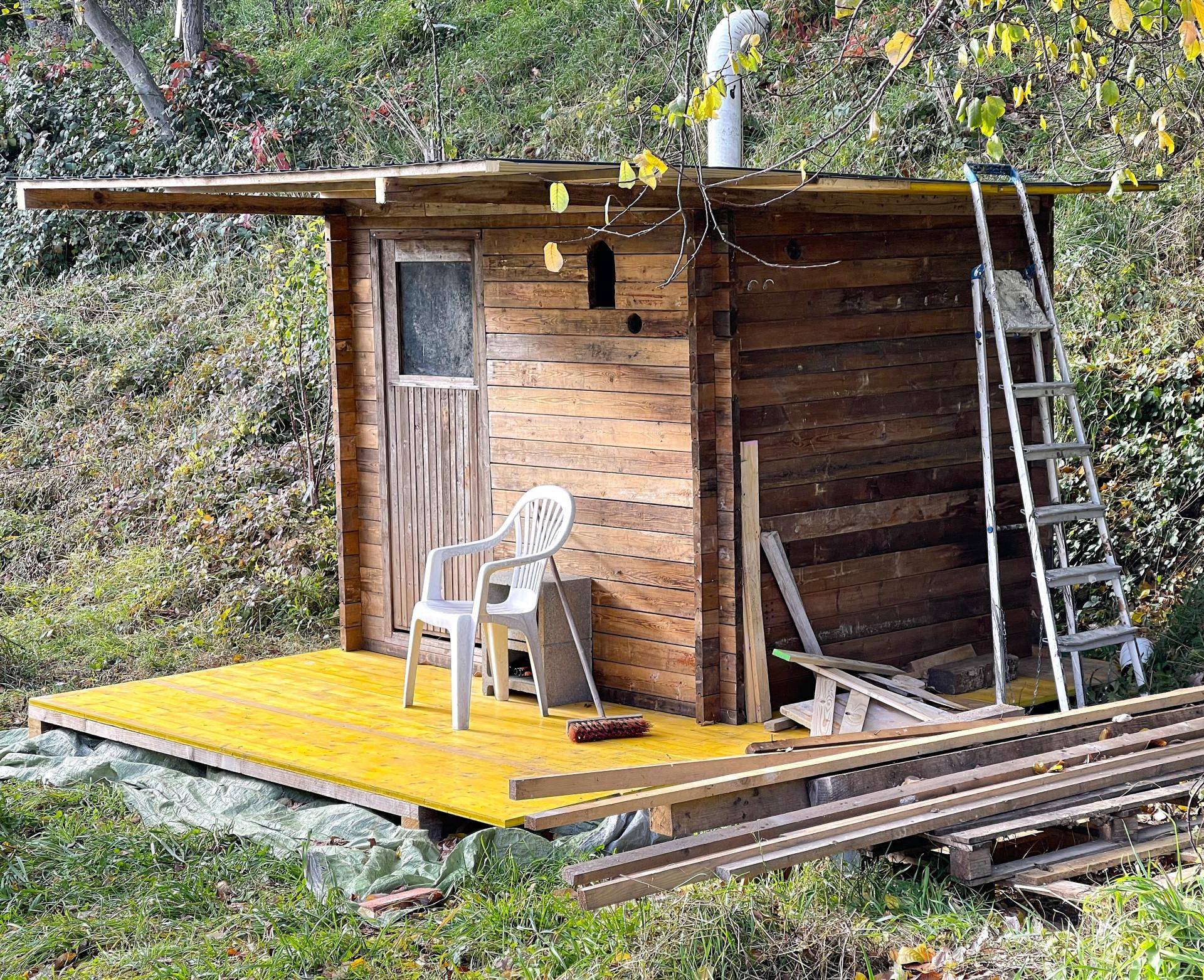 Rustikales Holzhaus im Grünen, möglicherweise eine Sauna oder ein Geräteschuppen.