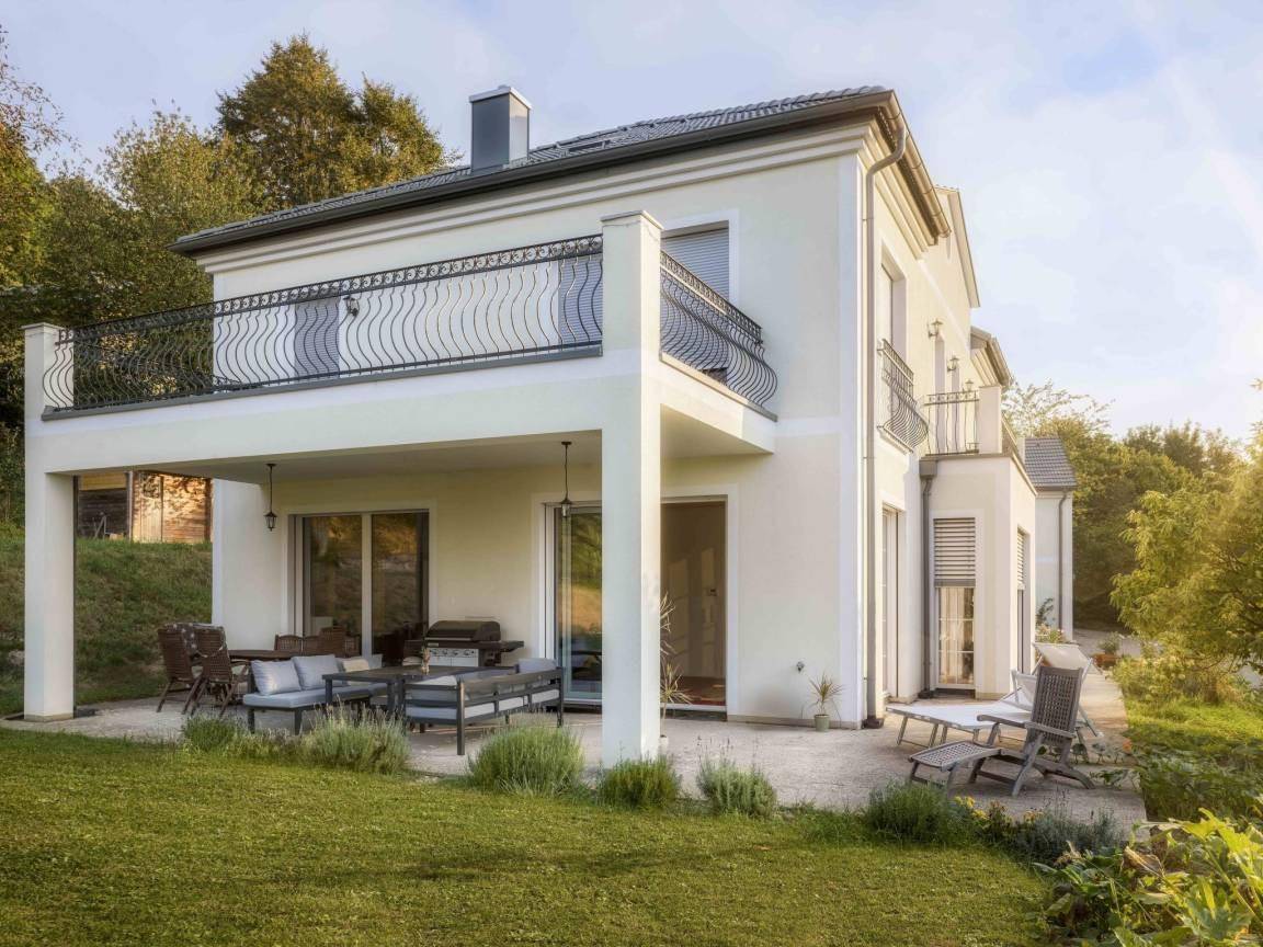 Große Terrasse mit Sitzgelegenheiten und Grillbereich, umgeben von Grün.