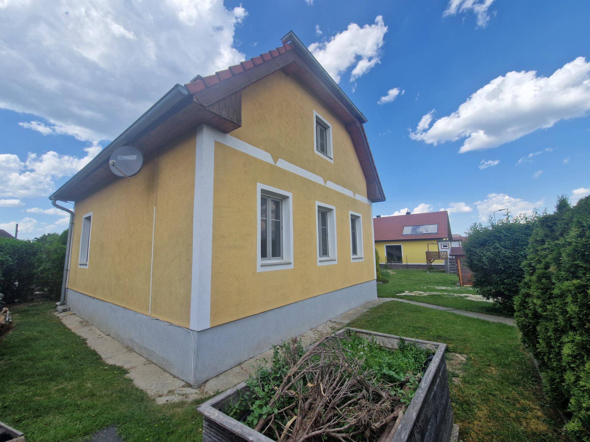 Seitenansicht des gelben Hauses mit Satellitenschüssel und grünem Gartenbereich.