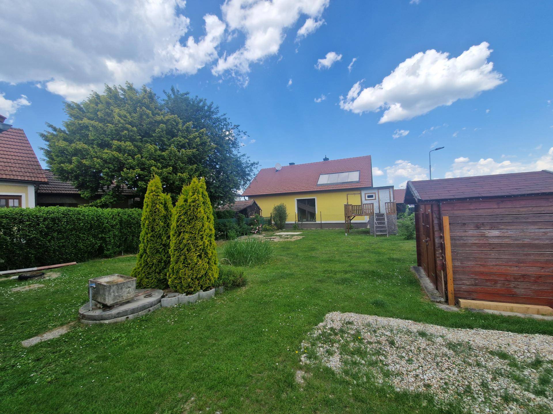 Großer Gartenbereich mit Rasen, Zierpflanzen und einem Holzschuppen im Hintergrund.