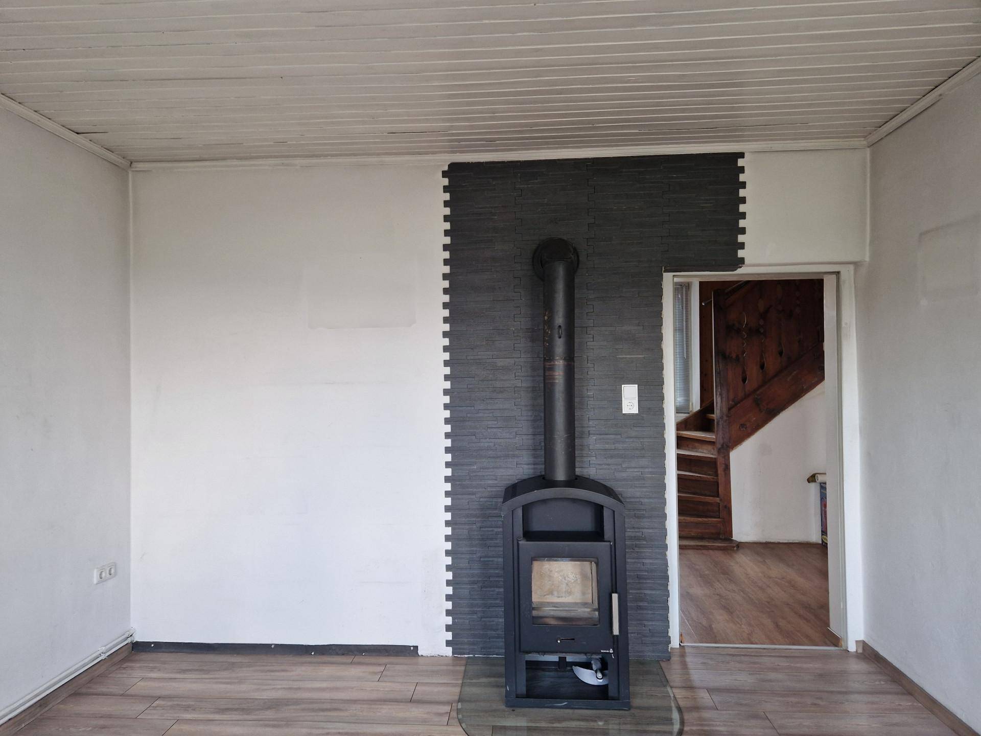 Gemütlicher Raum mit Holzofen, dekorativer Wandverkleidung und Zugang zur Holztreppe.