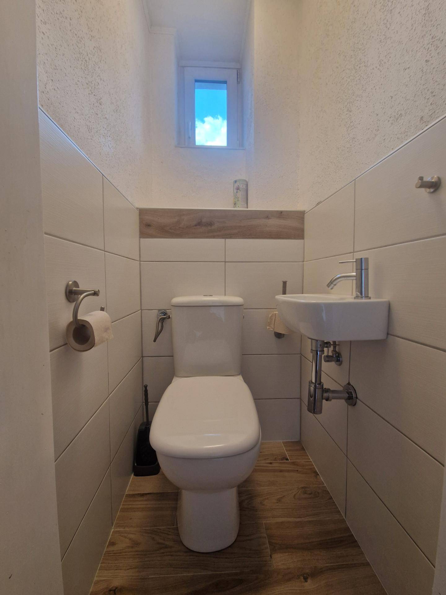 Modernes Gäste-WC mit weißen Fliesen, kleinem Waschbecken und Fenster.
