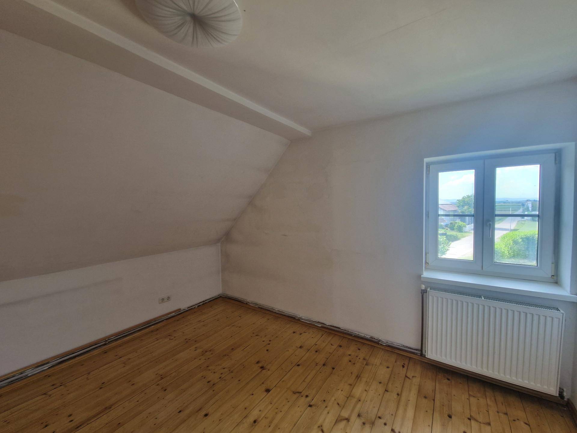 Helles Schlafzimmer im Dachgeschoss mit Holzdielenboden und schräger Decke.