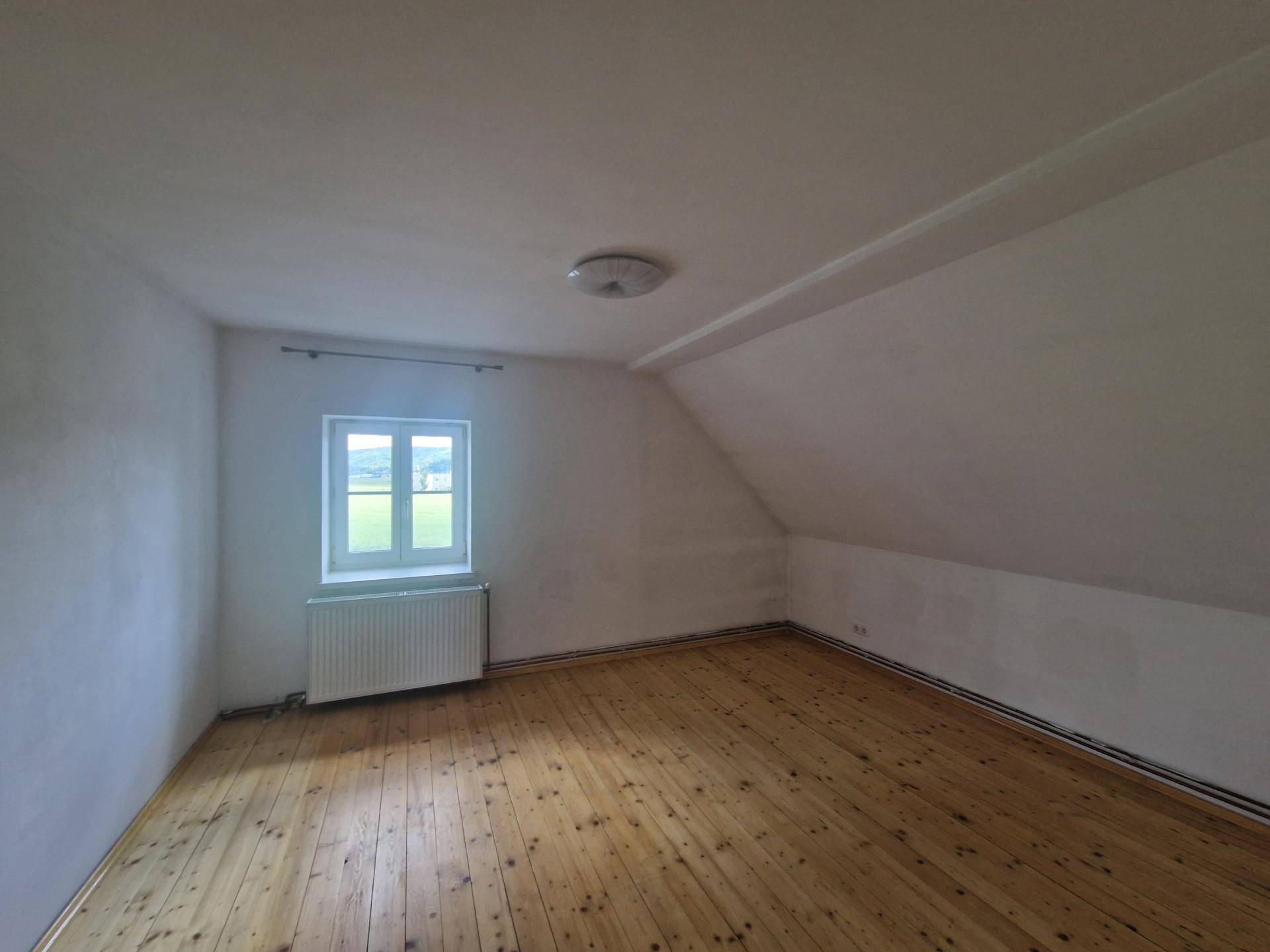 Geräumiges Zimmer im Dachgeschoss mit Holzdielenboden und schräger Decke.