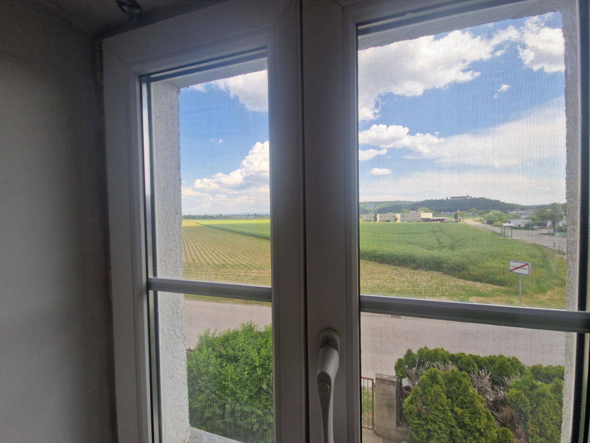 Fensterblick auf weite Felder und die hügelige Landschaft unter blauem Himmel.