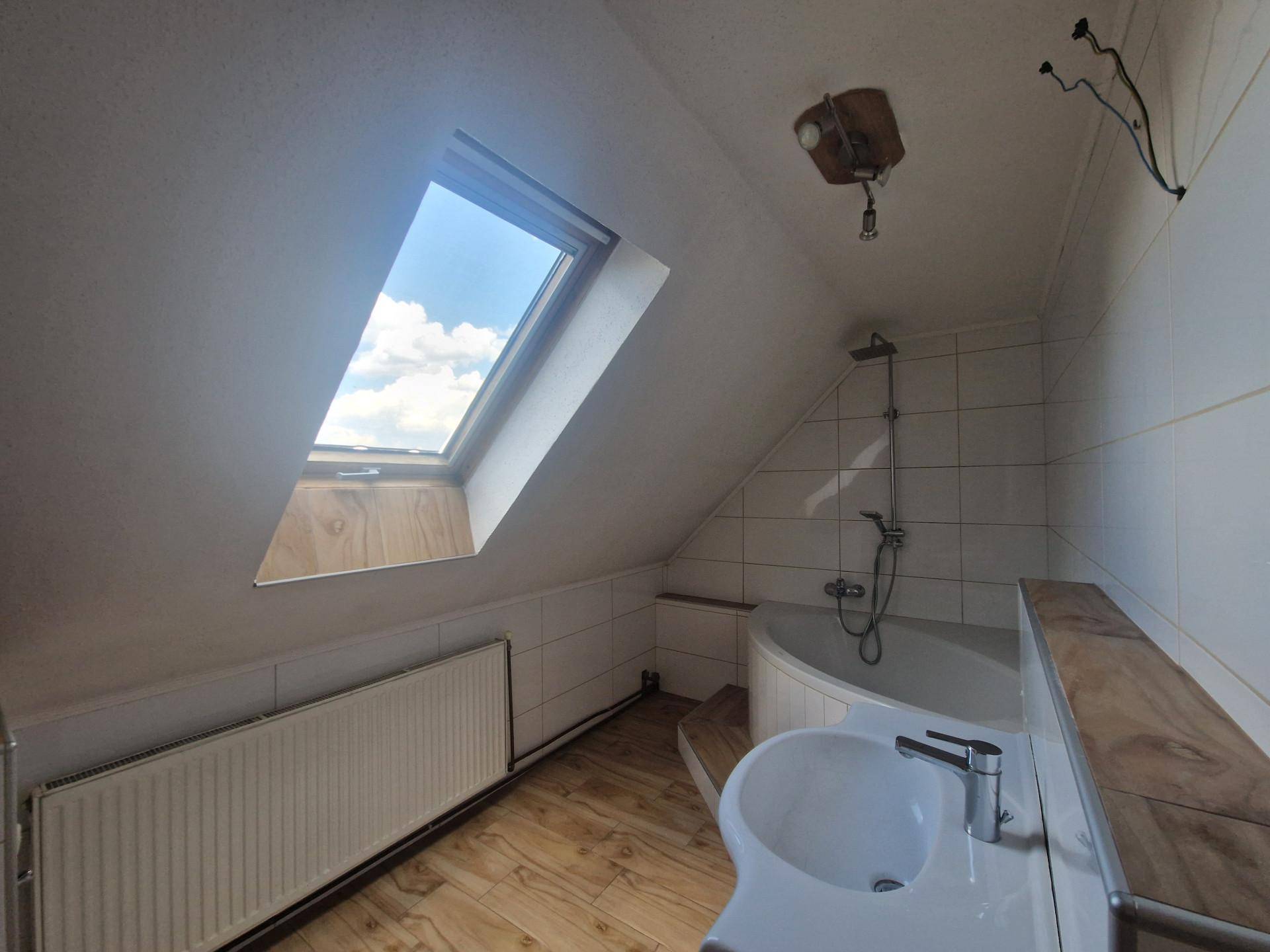 Helles Dachgeschossbad mit Badewanne, Waschbecken, Fliesen und Dachfenster.