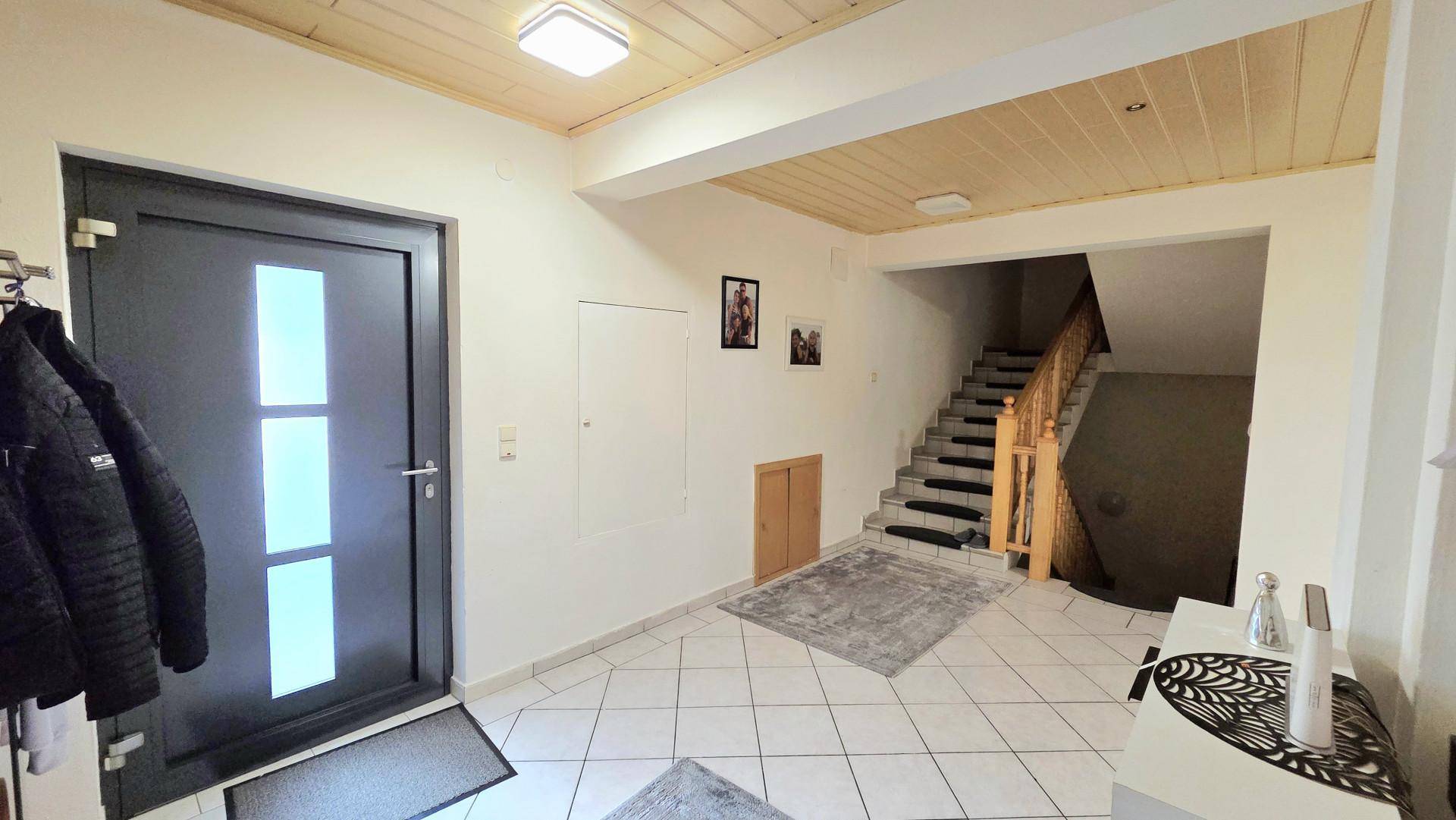 Eingangsbereich mit dunkler Haustür, gefliestem Boden und Treppe zum Obergeschoss.
