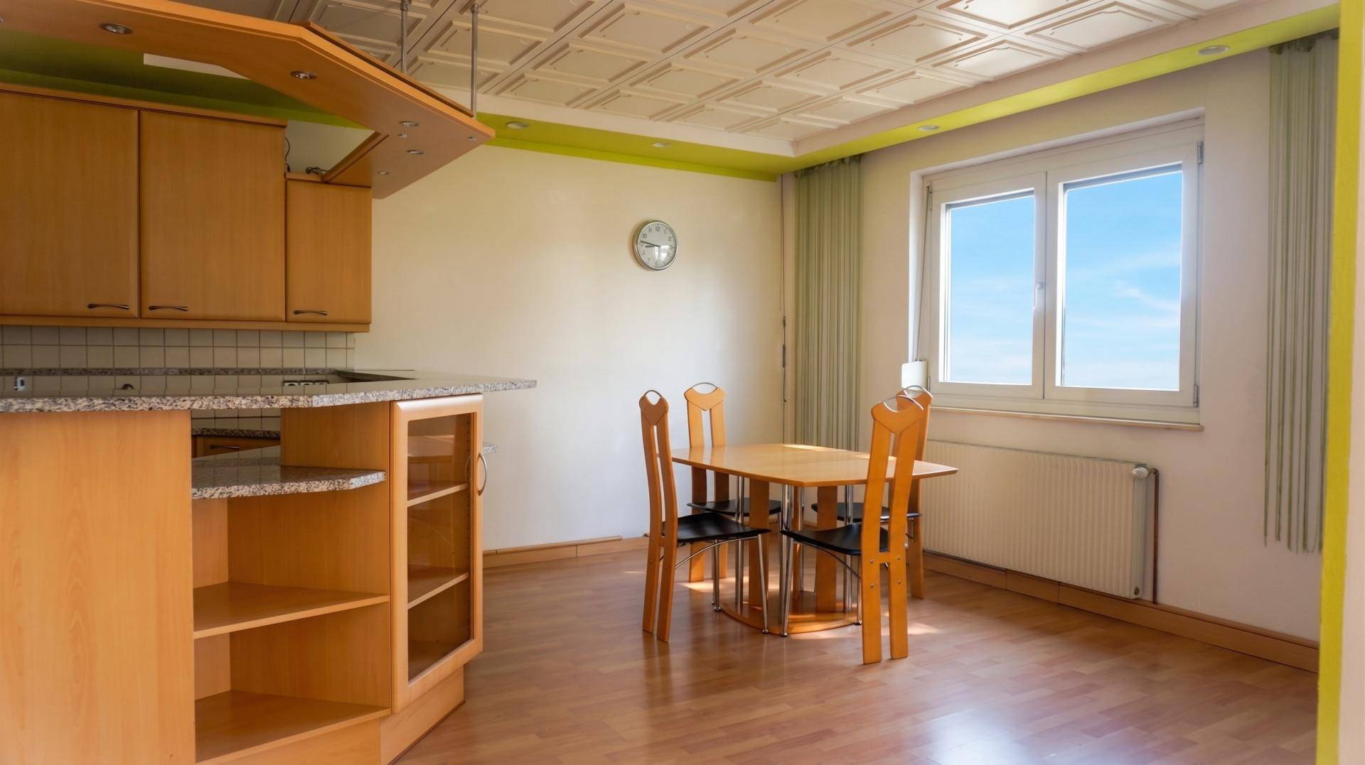 Essbereich in der Küche mit Holztisch, Stühlen und Fenster mit Blick ins Grüne.