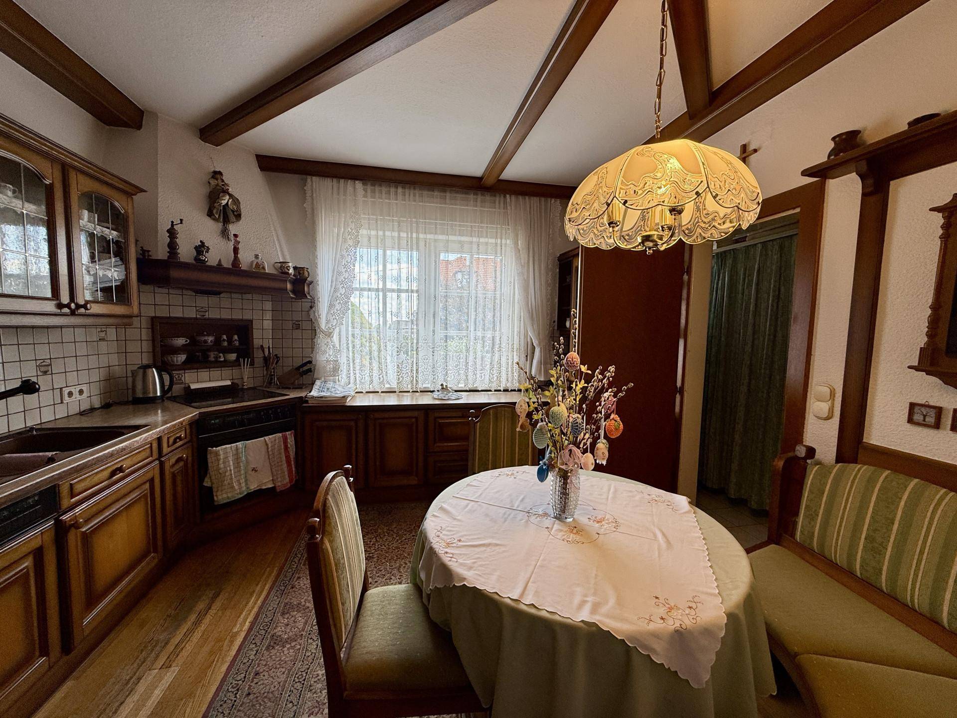 Gemütliche Wohnküche im Landhausstil mit Holzbalken, Esstisch und traditionellen Möbeln.