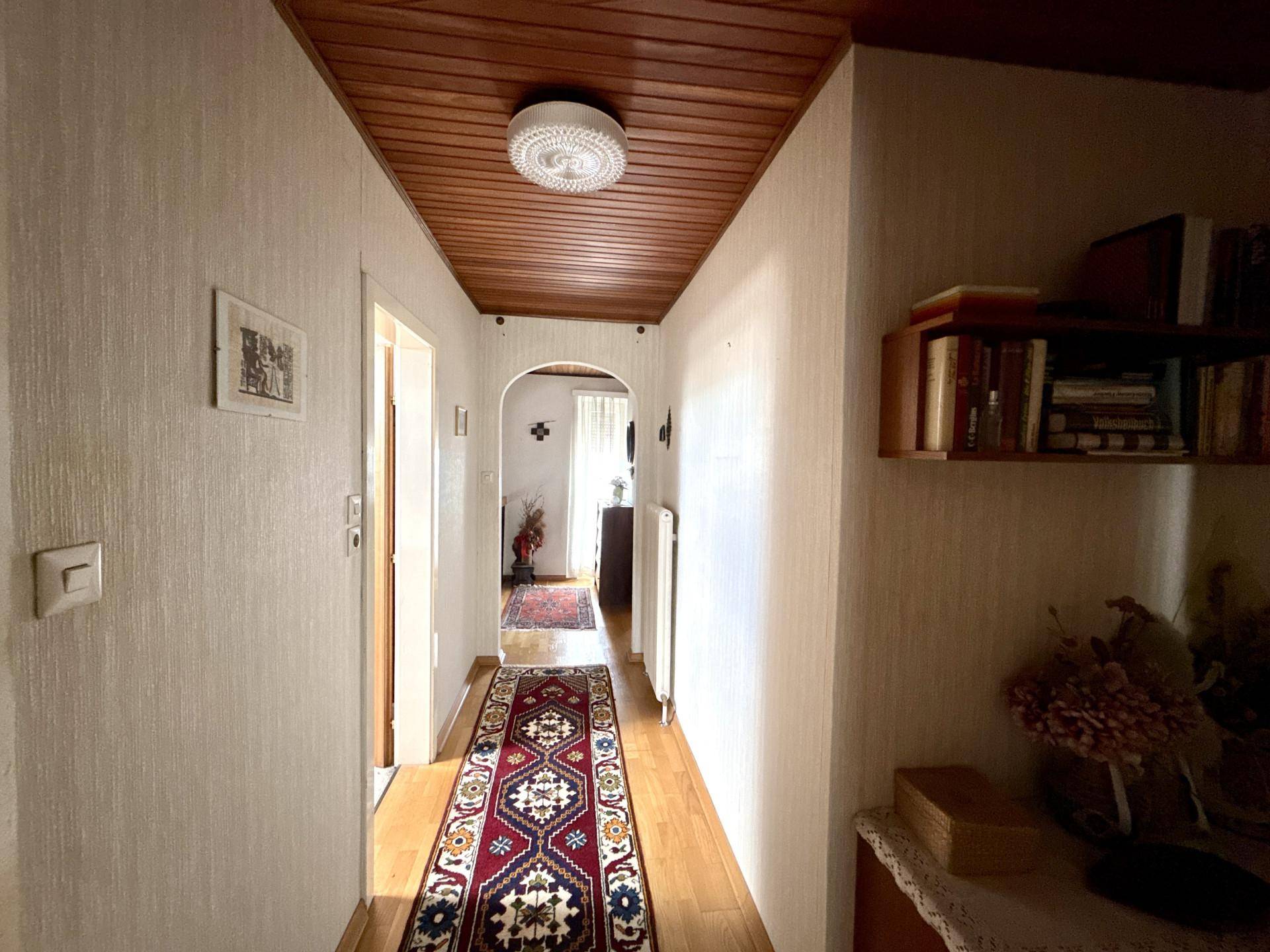 Langer Flur mit Holzdecke, Teppichläufer und Durchgang zu weiteren Räumen.