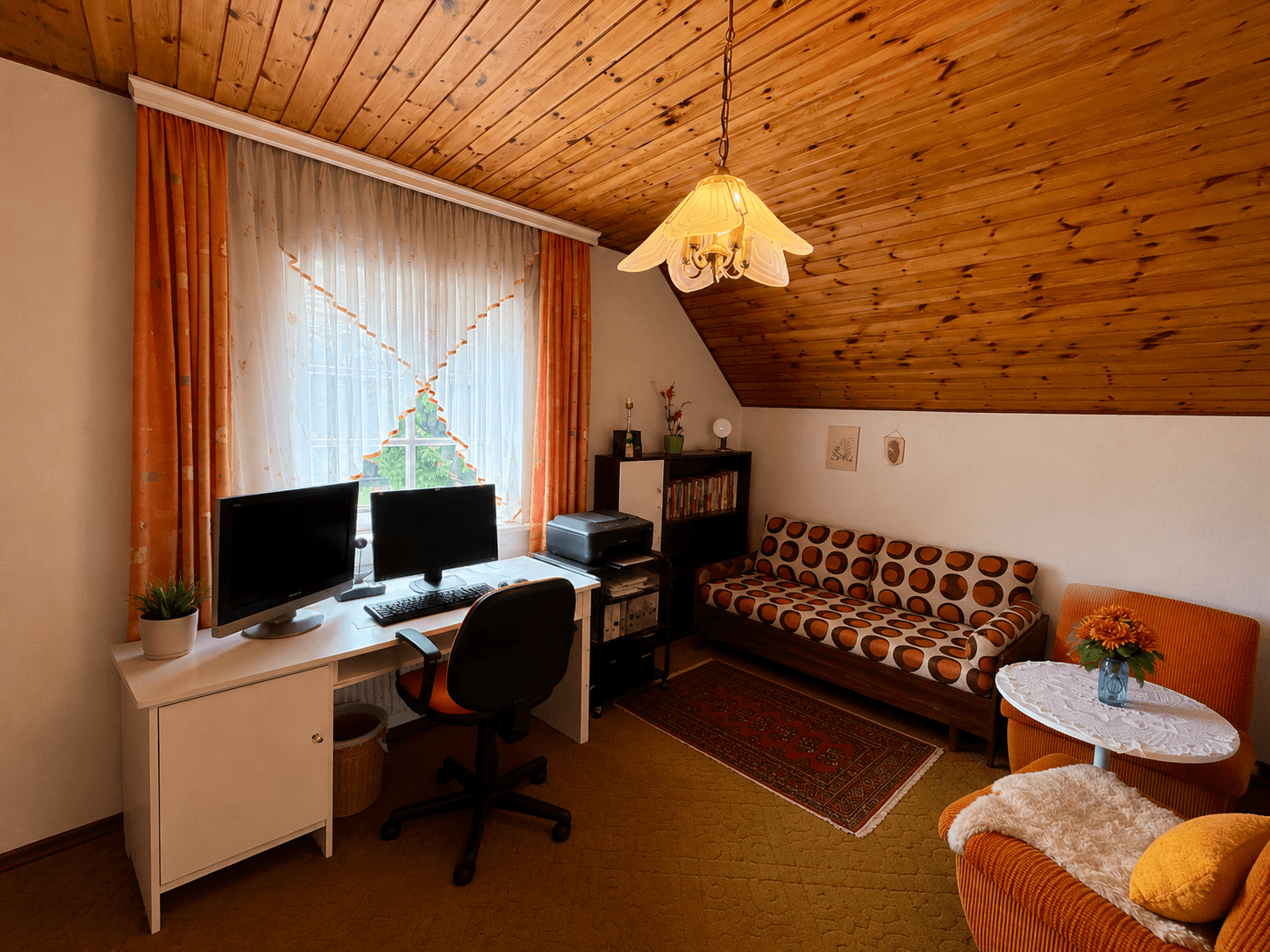 Arbeitszimmer mit Holzdecke, Schreibtisch, Sofa und Fenster mit Blick ins Grüne.