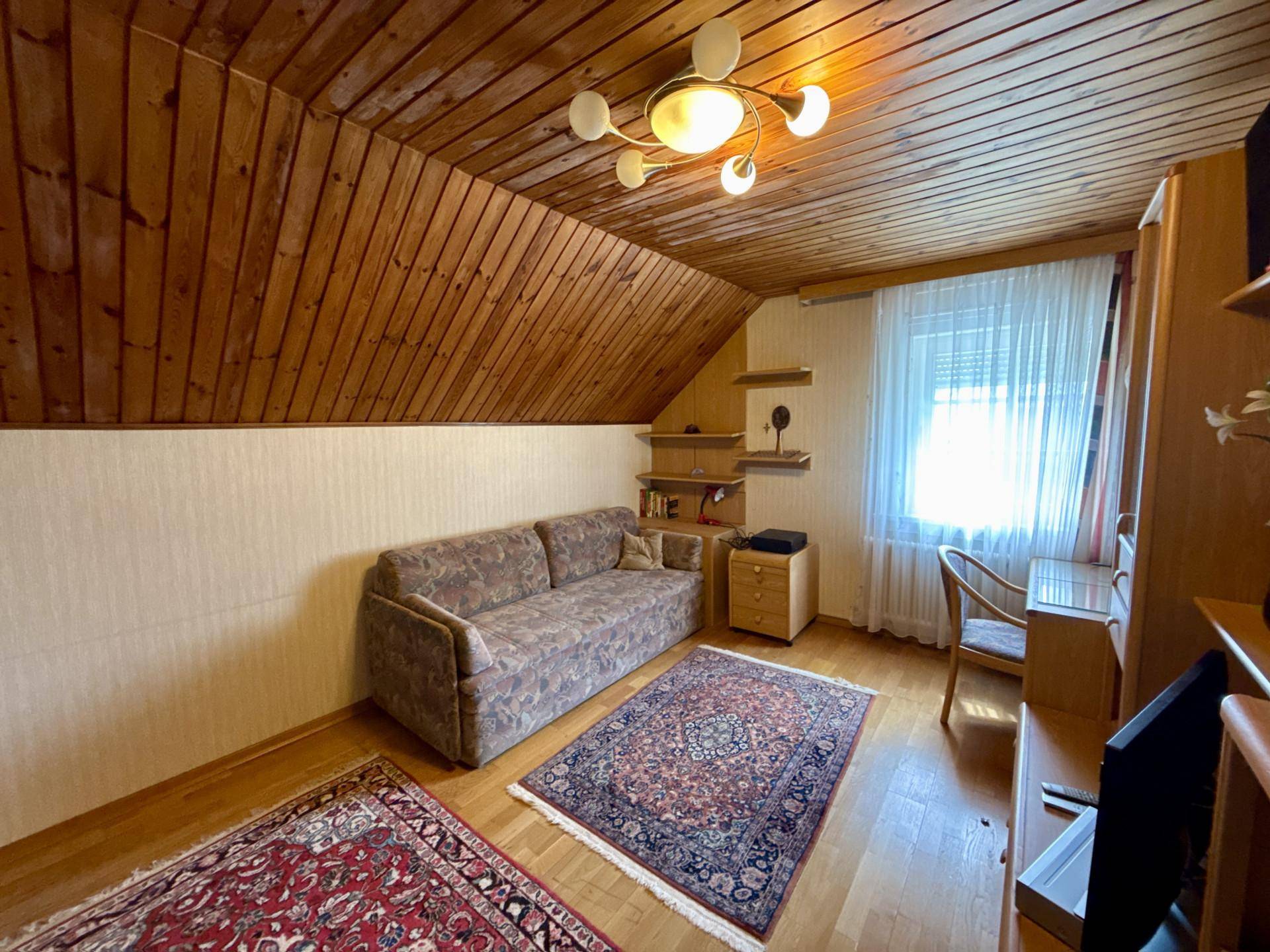 Gemütliches Schlafzimmer mit Holzdecke, Sofa und Teppichboden unter einer Dachschräge.