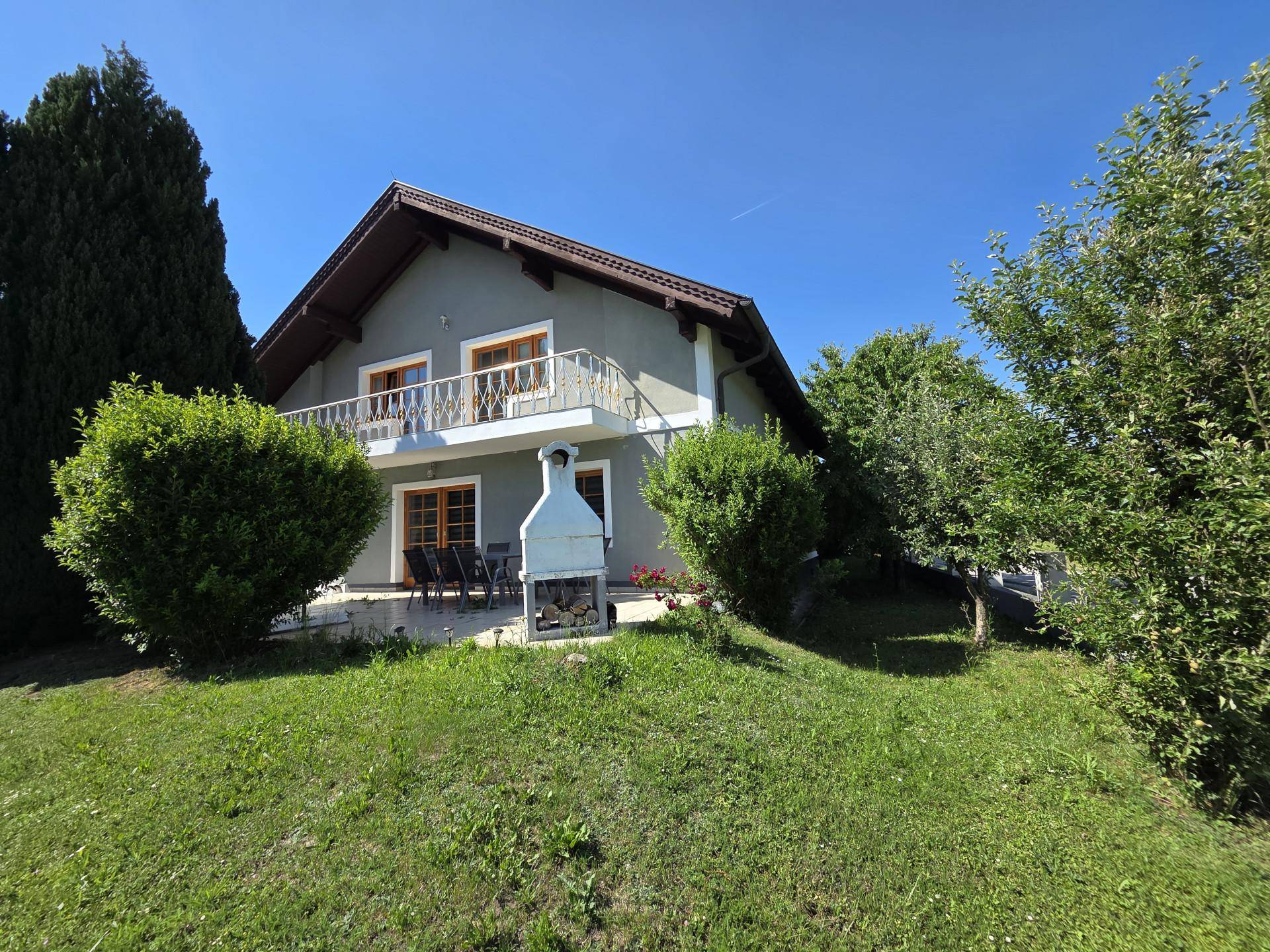 Ansicht des Hauses von der Gartenseite mit Rasenfläche, Außengrill und Sitzgelegenheiten im Freien.