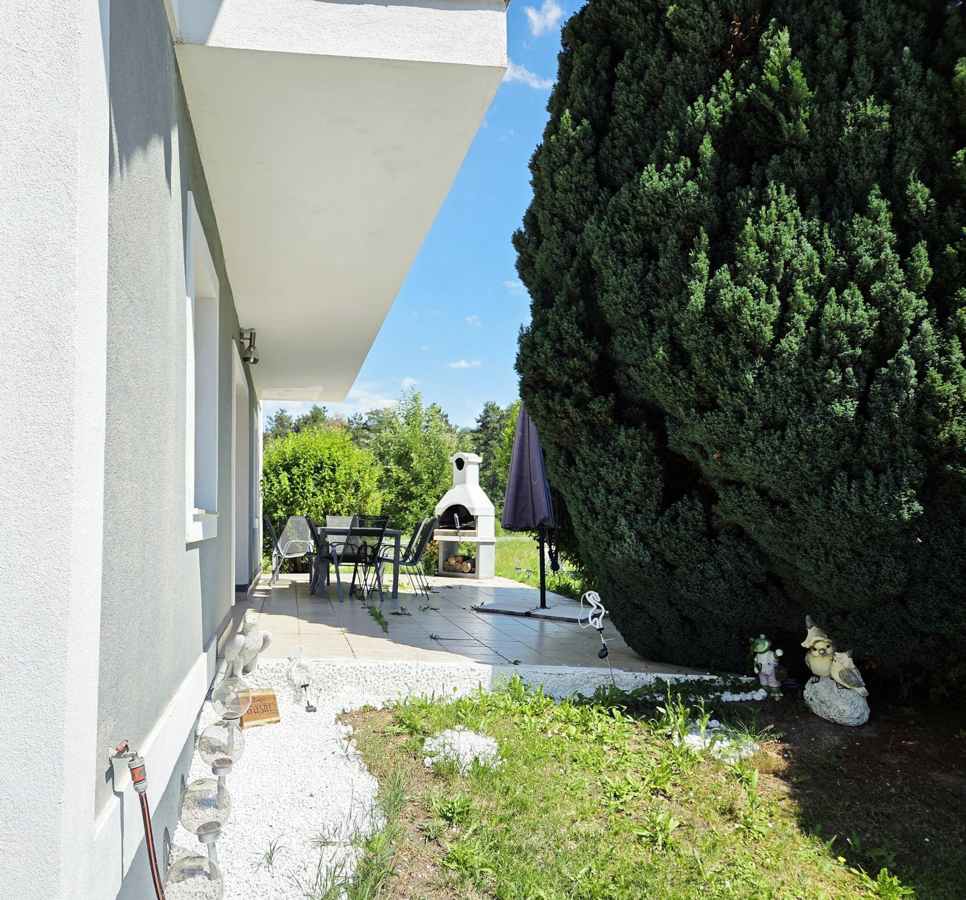 Gemütliche Terrasse mit Außengrill, Esstisch und Stühlen, umgeben von Grünflächen.