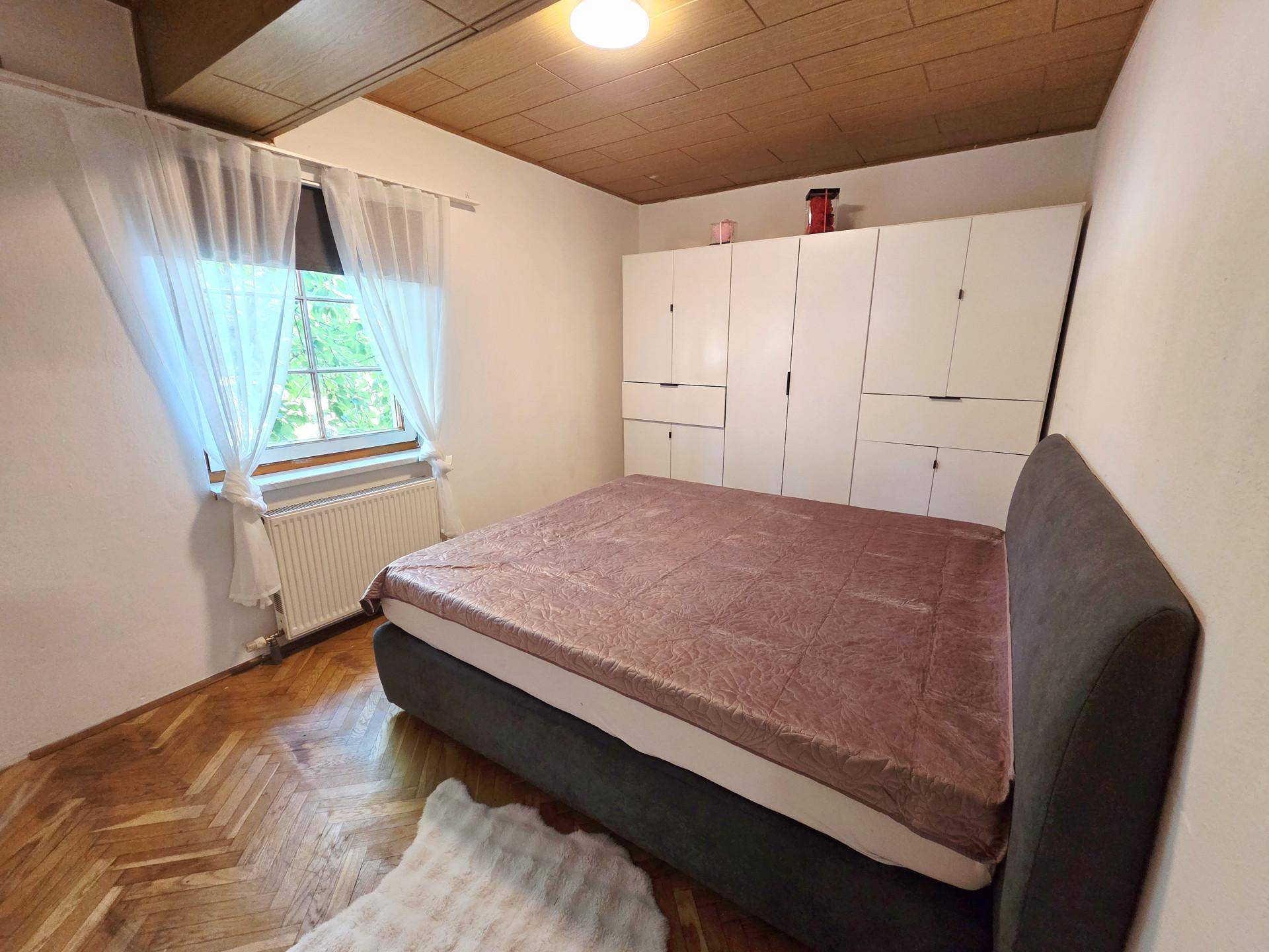 Schlafzimmer mit Holzboden, großem Bett und weißen Einbauschränken, hell durch ein Fenster.