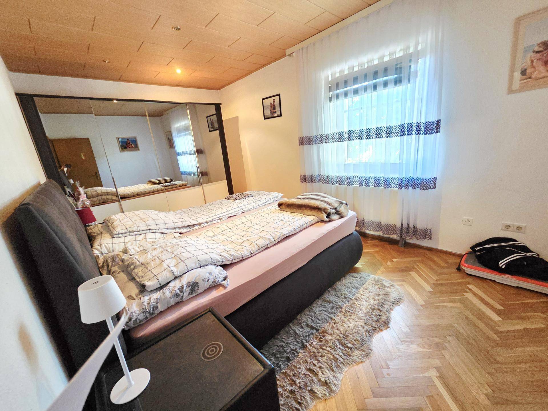 Schlafzimmer mit Holzboden, großem Bett und Spiegelschränken, hell durch ein großes Fenster.
