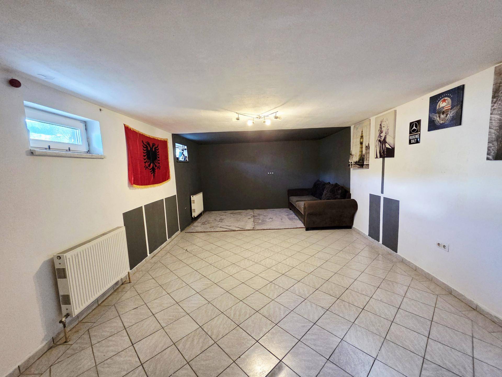 Geräumiger Kellerraum mit Fliesenboden, Heizkörpern und einer dunklen Akzentwand, als Wohnraum nutzbar.