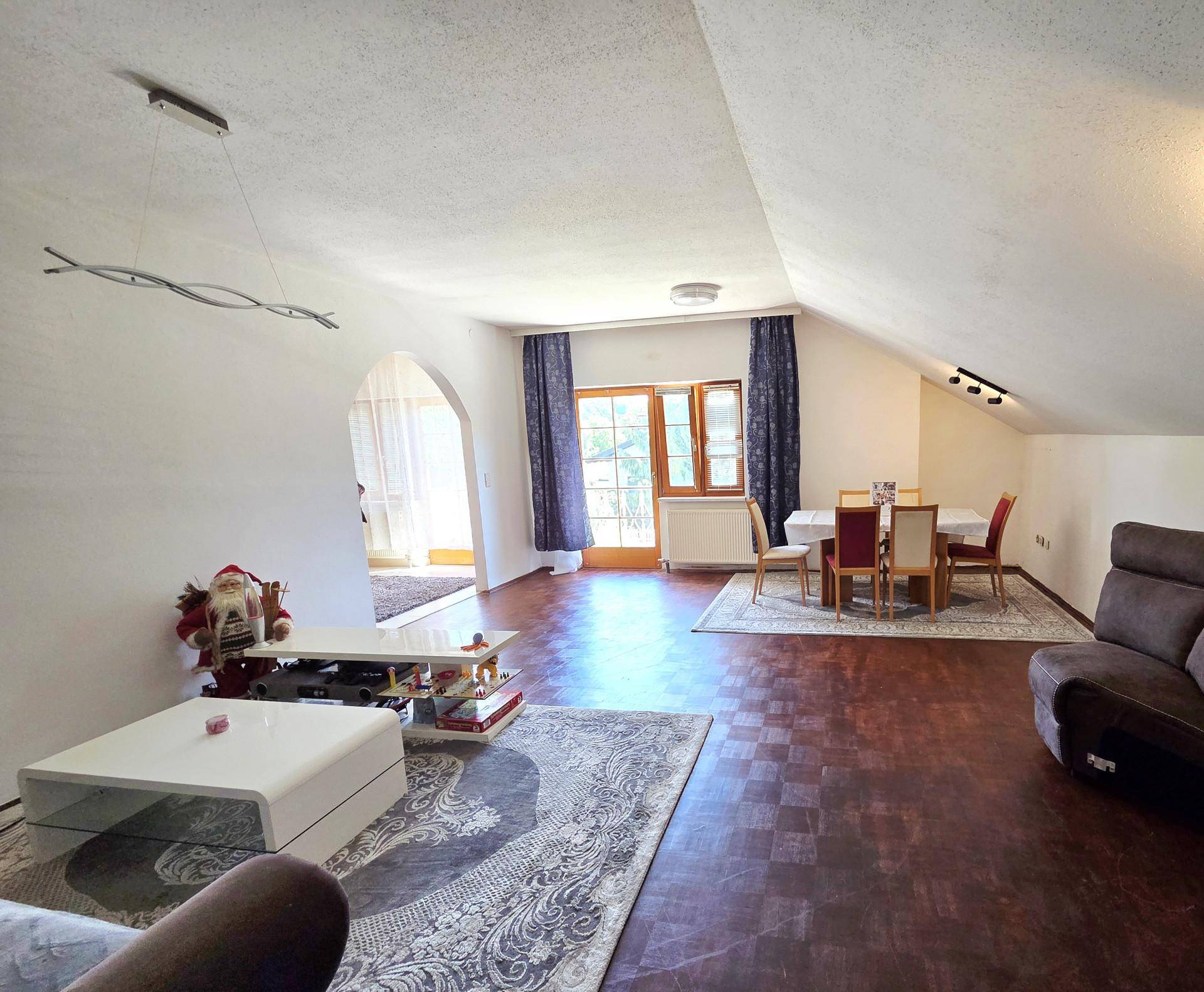 Offener Wohn-Essbereich im Dachgeschoss mit Holzboden, Esstisch und Sofa, Zugang zum Balkon.