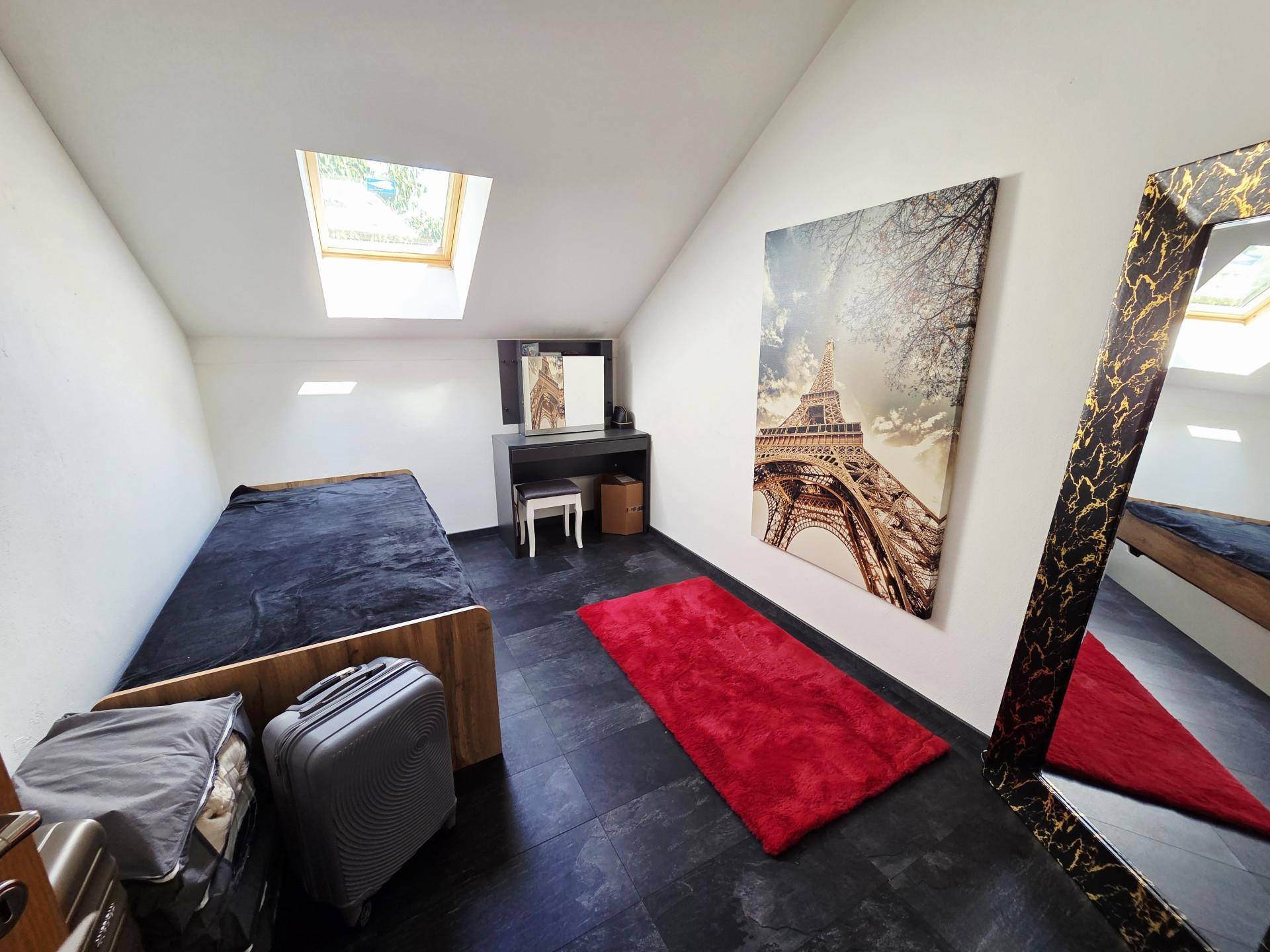 Schlafzimmer im Dachgeschoss mit Einzelbett, dunklem Boden und Dachfenster für natürliches Licht.