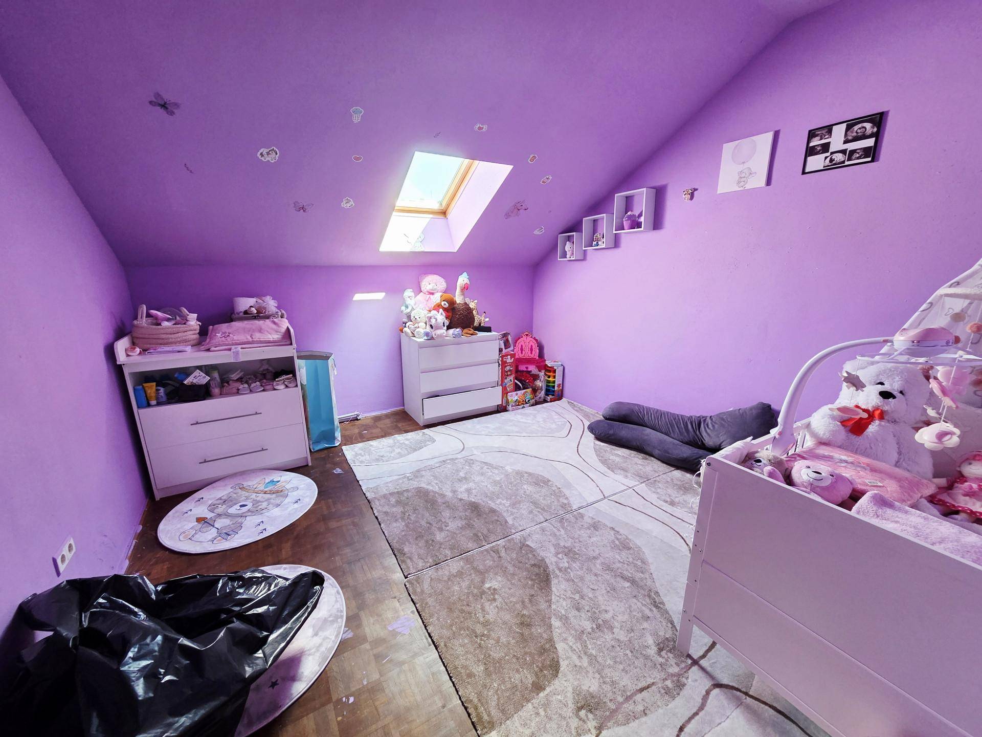 Kinderzimmer im Dachgeschoss mit lila Wänden, Dachfenster und Babybett, hell und freundlich.